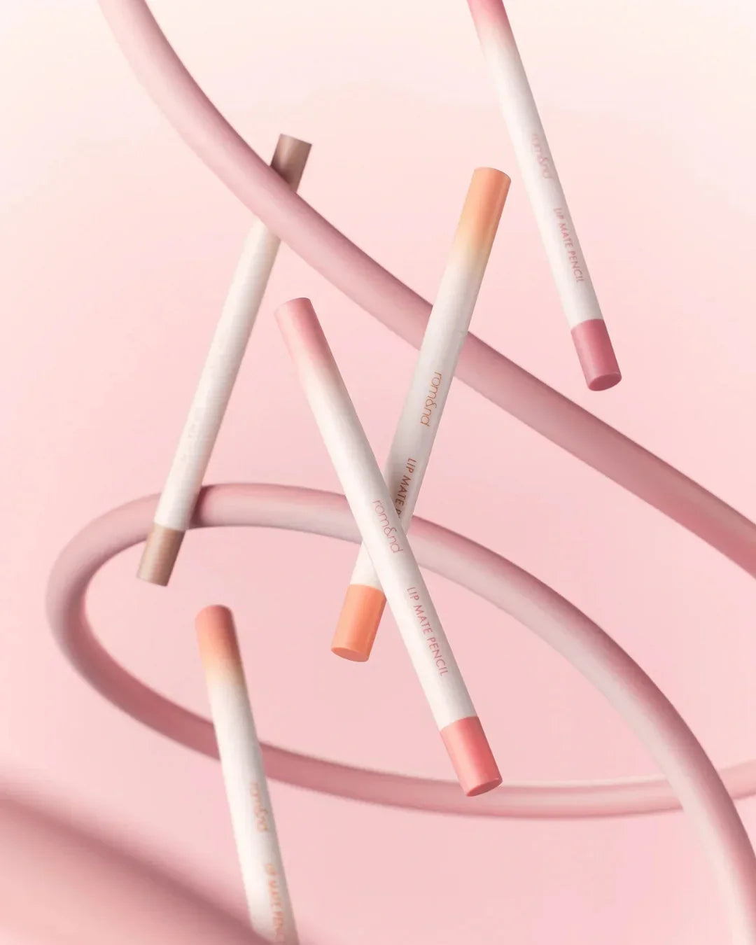 Lip Mate Pencil set in pastel pink and peach shades floating with pink swirls on a soft pink background