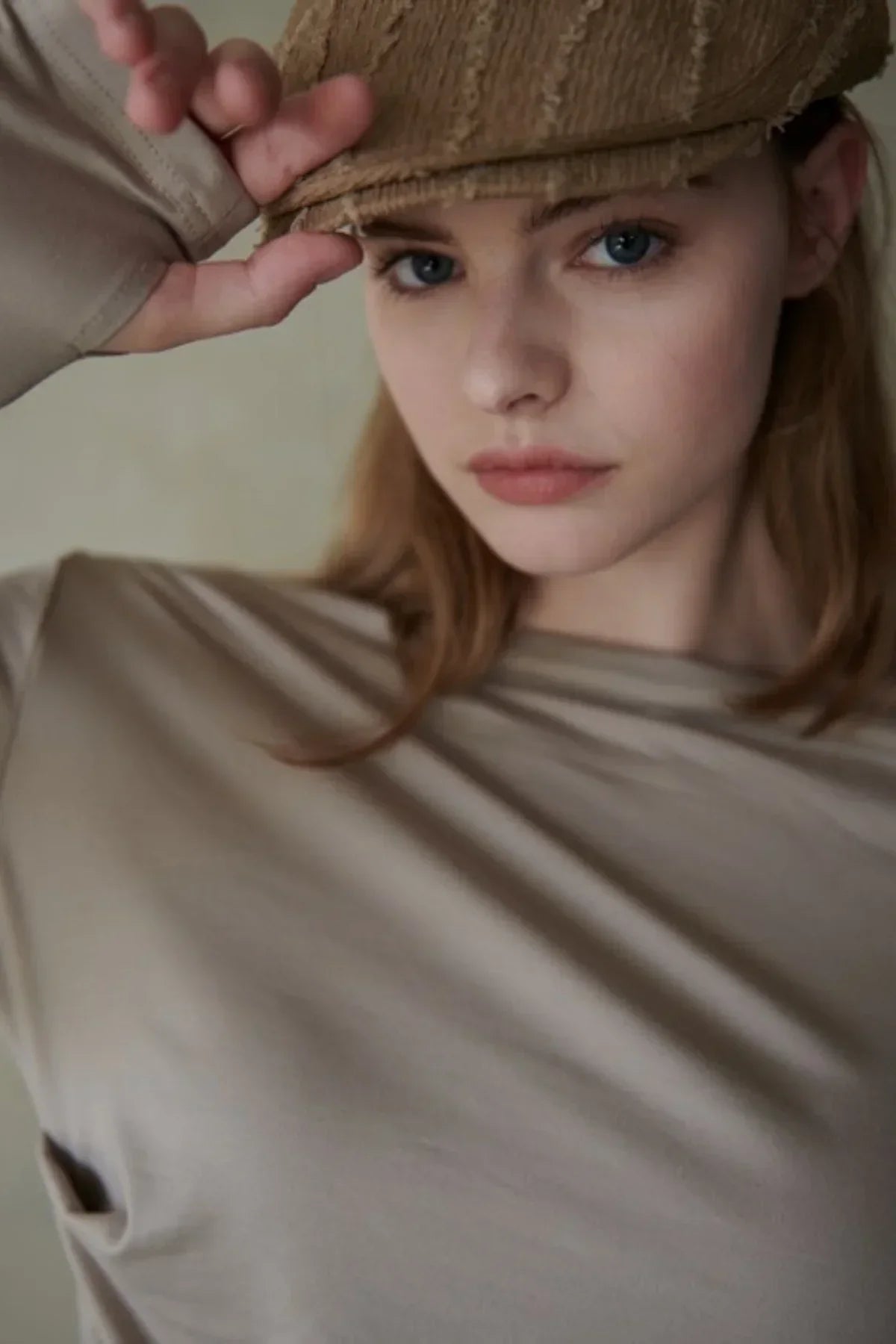 Close-up of woman wearing beige long-sleeved shirt and brown textured cap, posing indoors