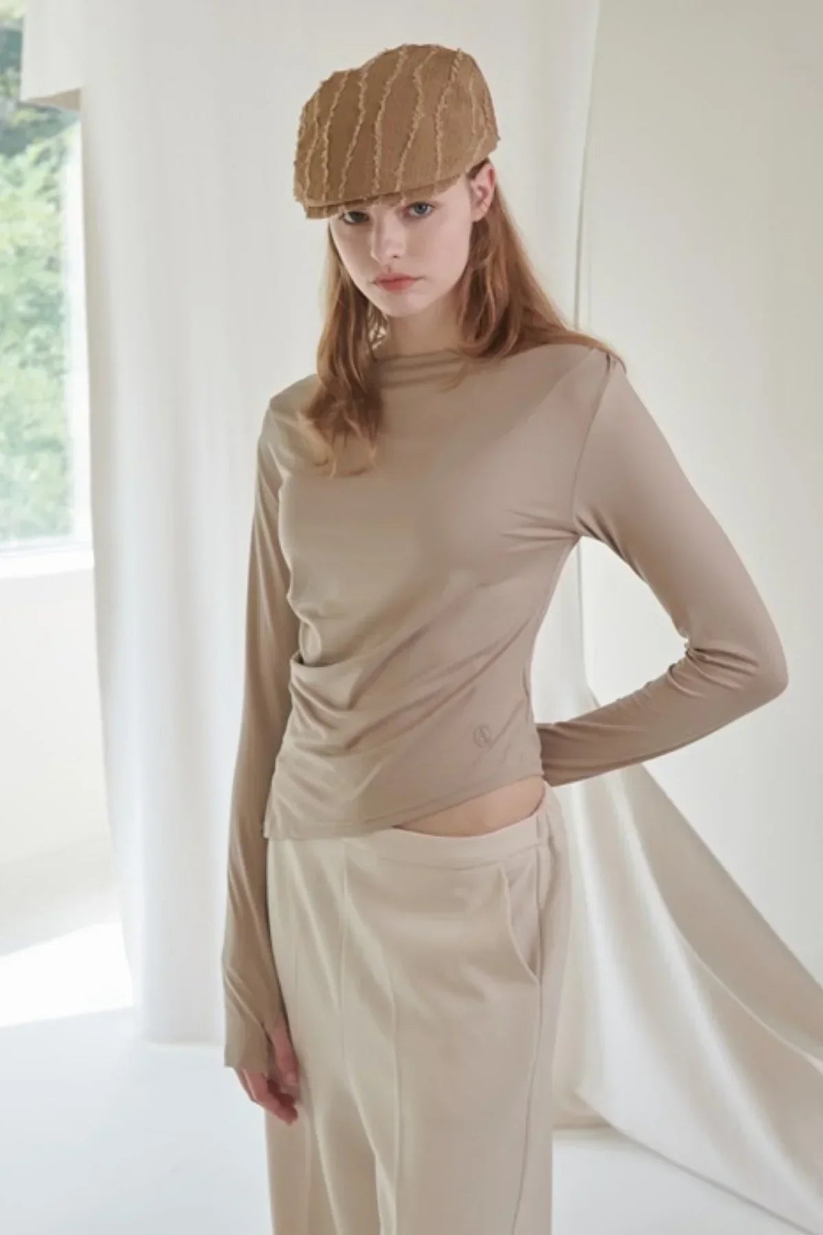 Model wearing beige long-sleeve fitted top and matching pants with textured beige cap in studio