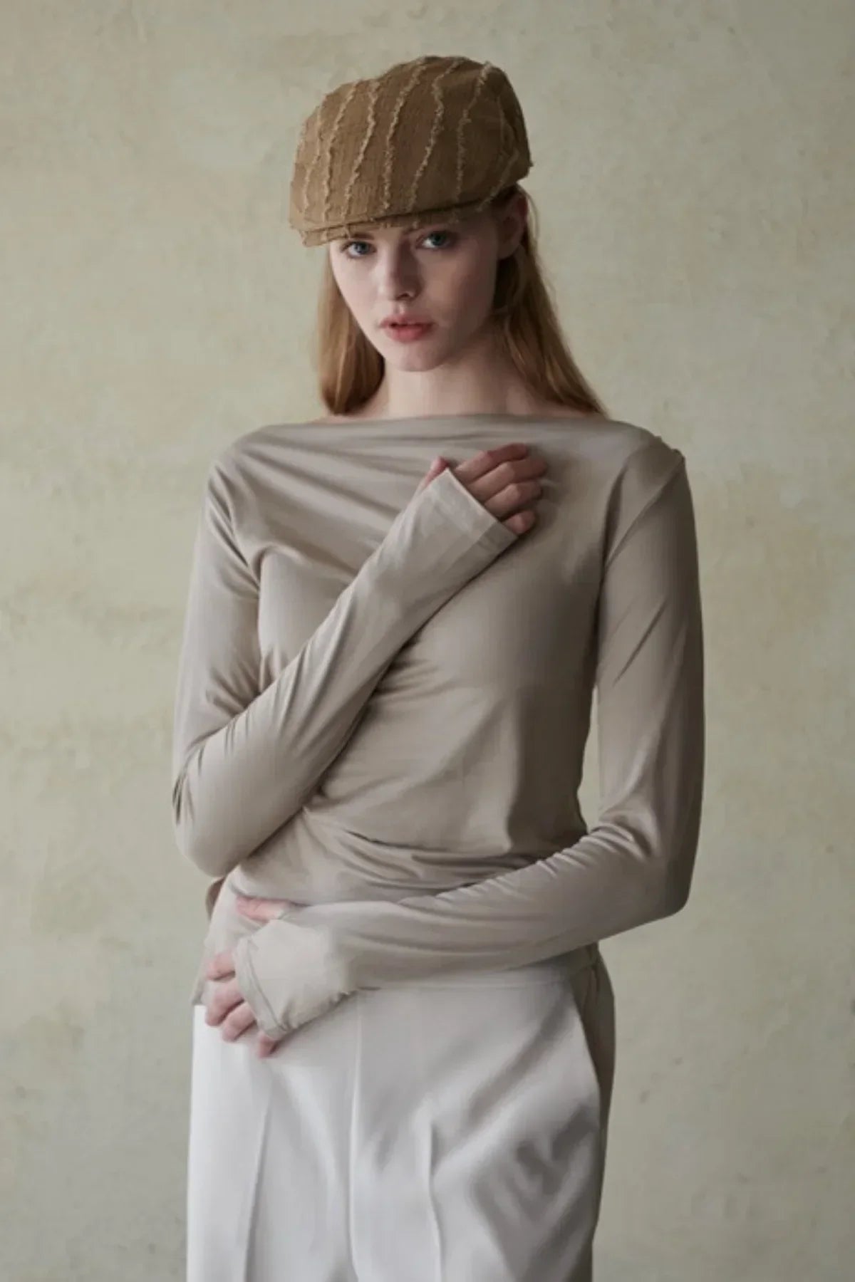 Woman wearing beige long-sleeve top and textured brown beret against neutral background