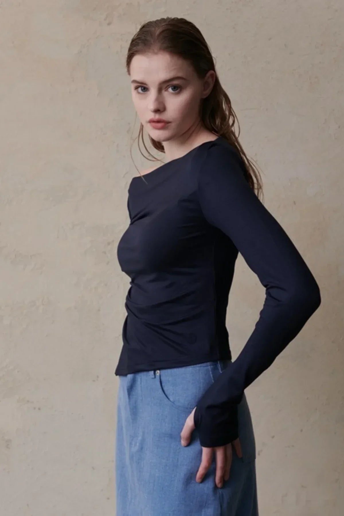 Woman wearing navy blue long-sleeve fitted top and light blue denim skirt against beige wall