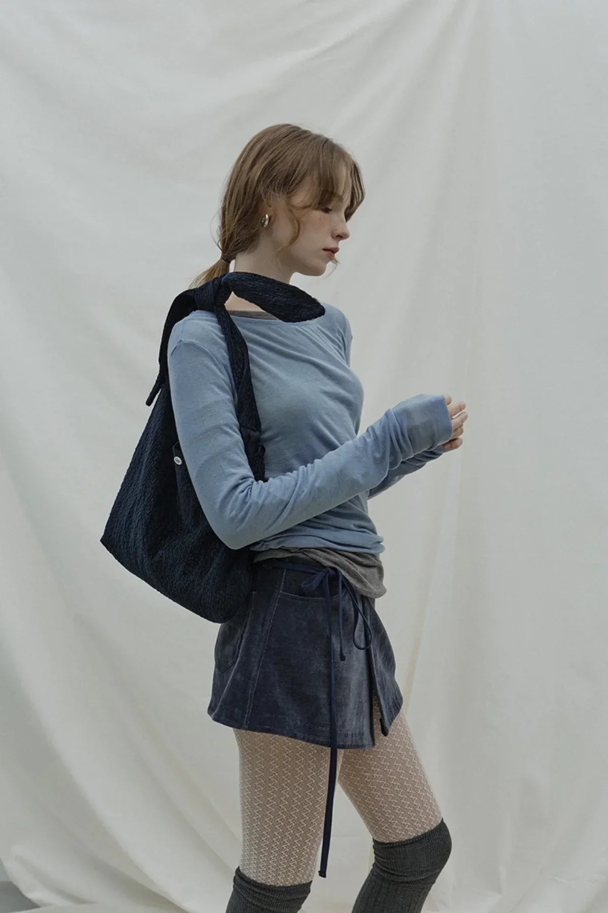 Woman wearing cloudy blue long-sleeve top with black bag, navy skirt, patterned tights, and knee-high socks