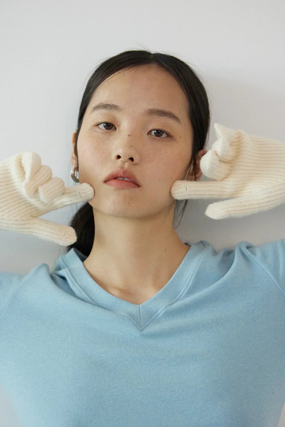 Woman wearing cream-colored knitted gloves and light blue top posing against plain background