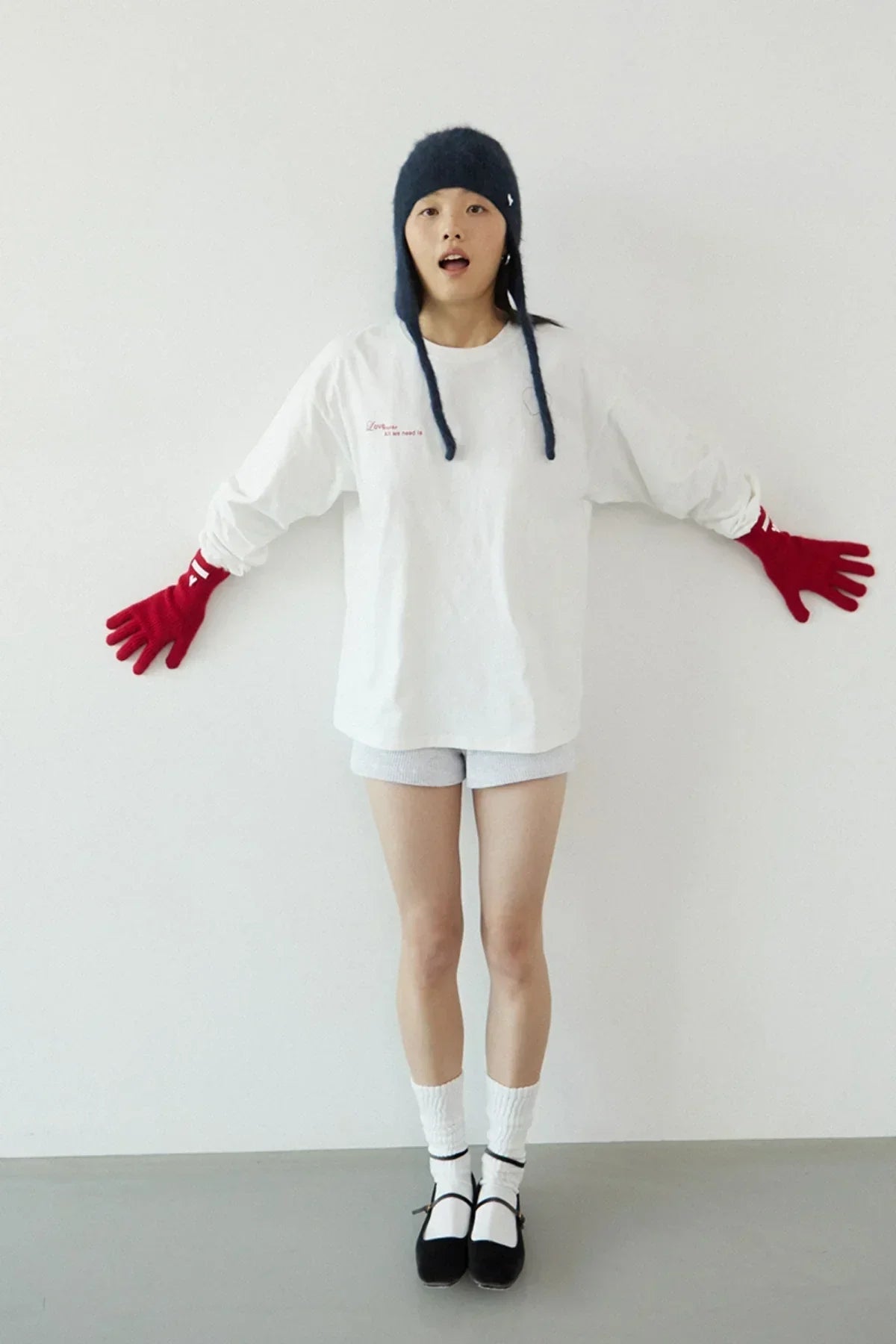 Woman in white long-sleeve shirt, gray shorts, black hat with earflaps, red gloves, white socks, and black shoes