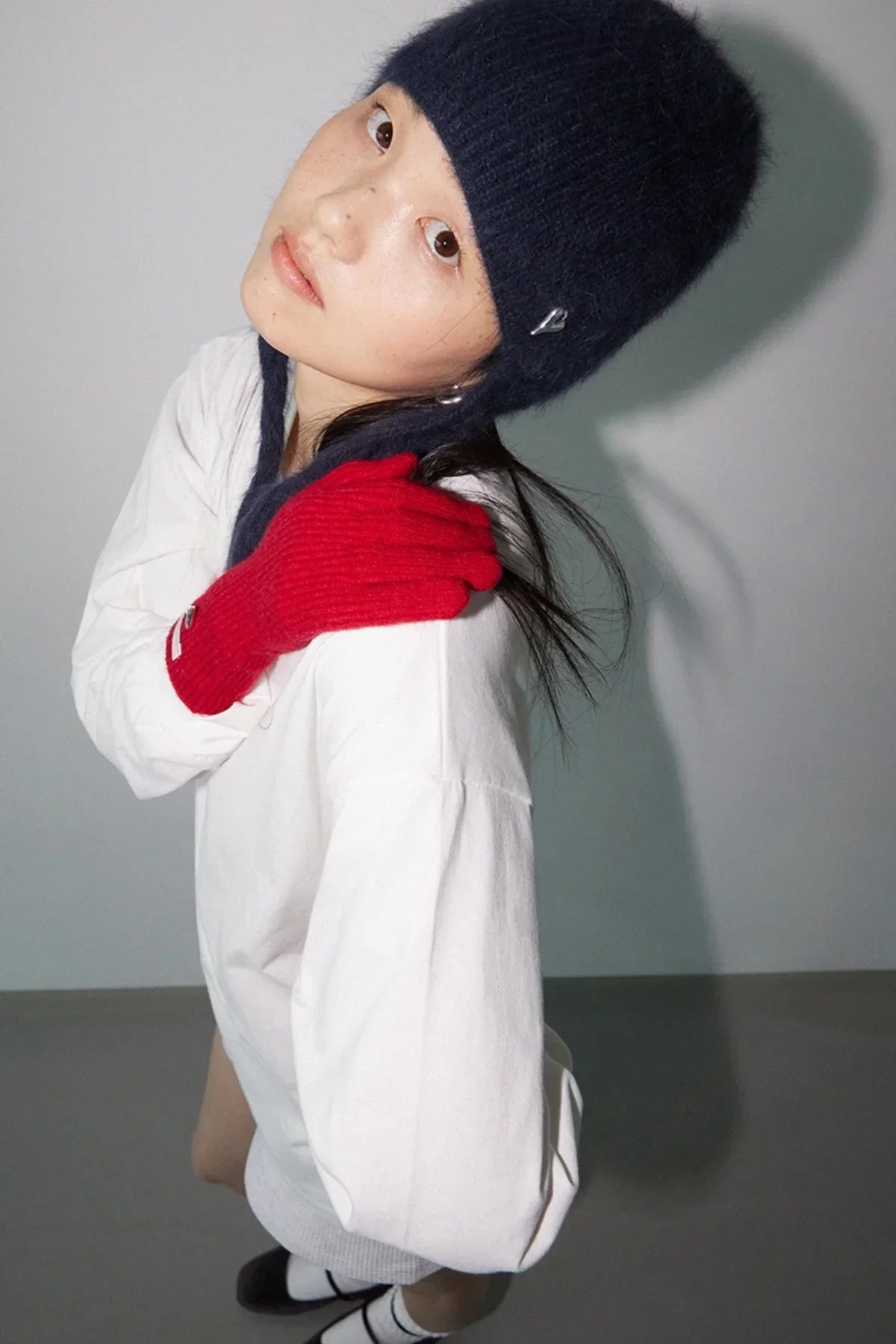 Young woman wearing a navy knitted hat and bright red gloves posing in white top and black shoes