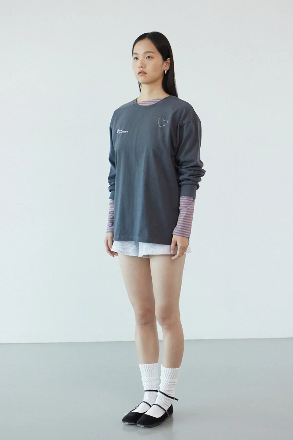 Model wearing dark gray Love More long-sleeve t-shirt with heart print, layered over striped sleeves