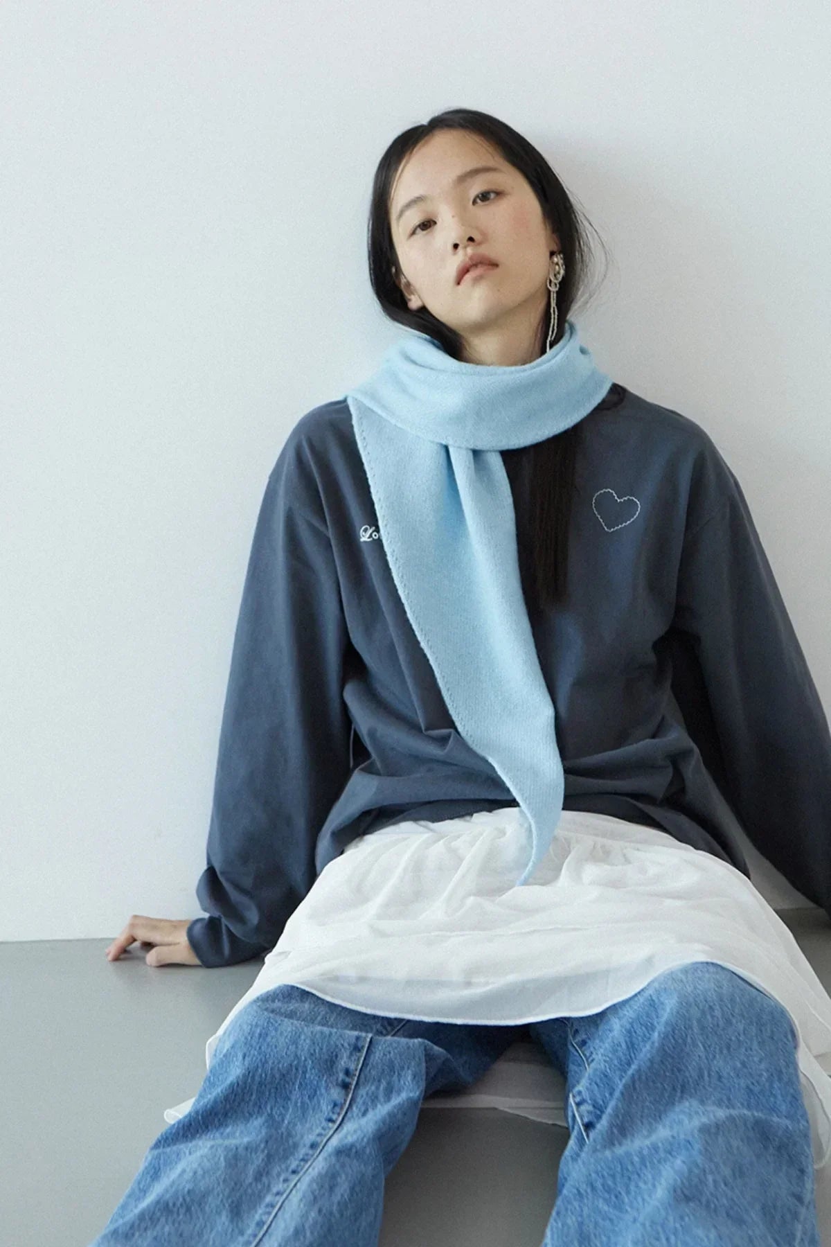 Woman wearing dark gray Love More sweatshirt with heart detail and light blue scarf, casual jeans outfit