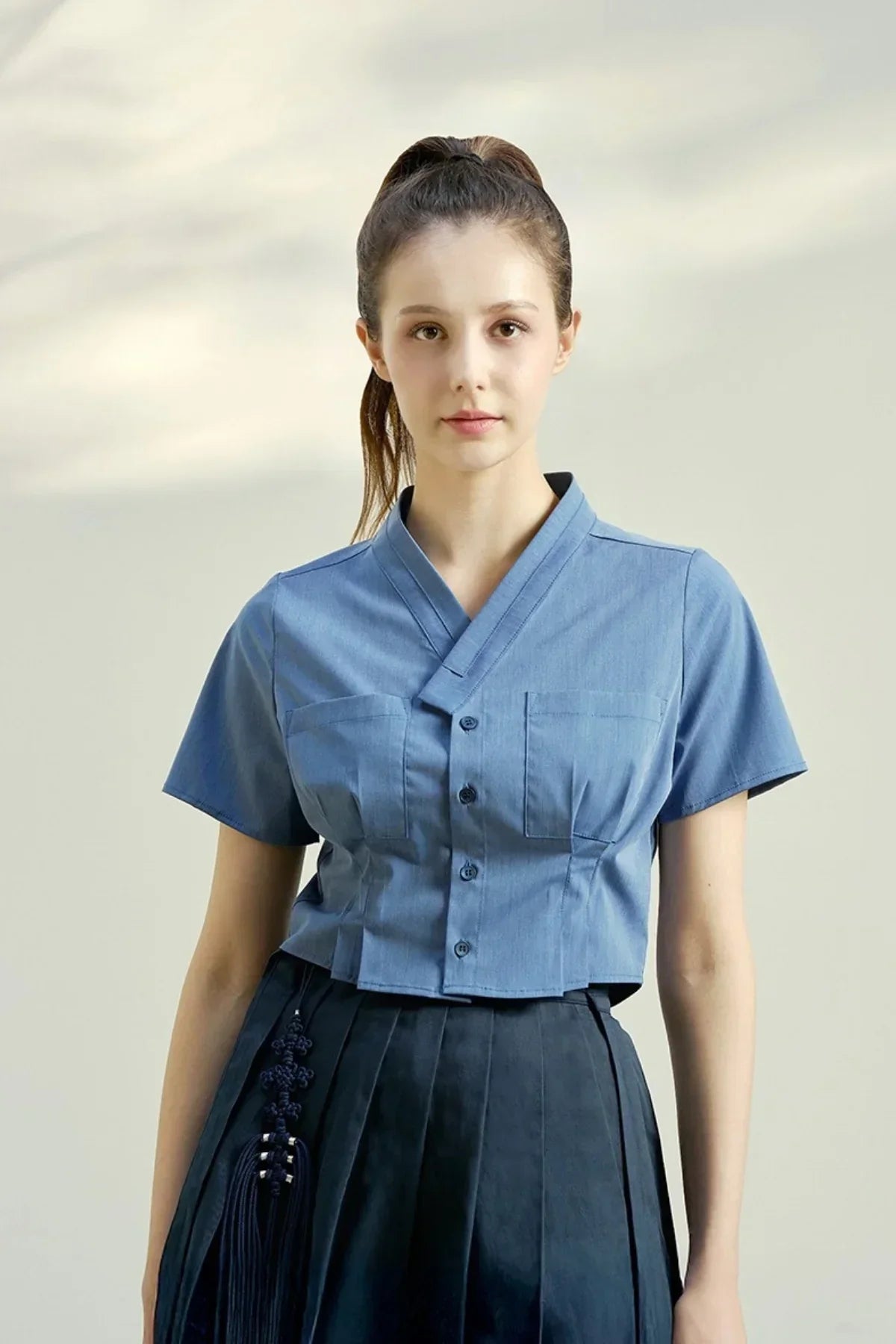 Young woman wearing indigo blue short-sleeve blouse with button details and pleated black skirt