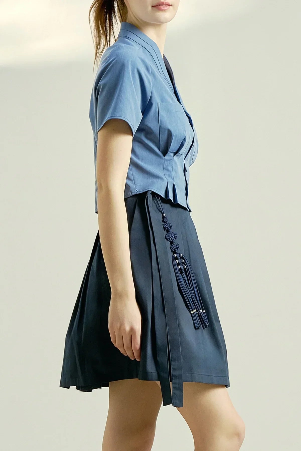 Woman wearing indigo blue short-sleeve blouse and navy pleated skirt with tassel detail