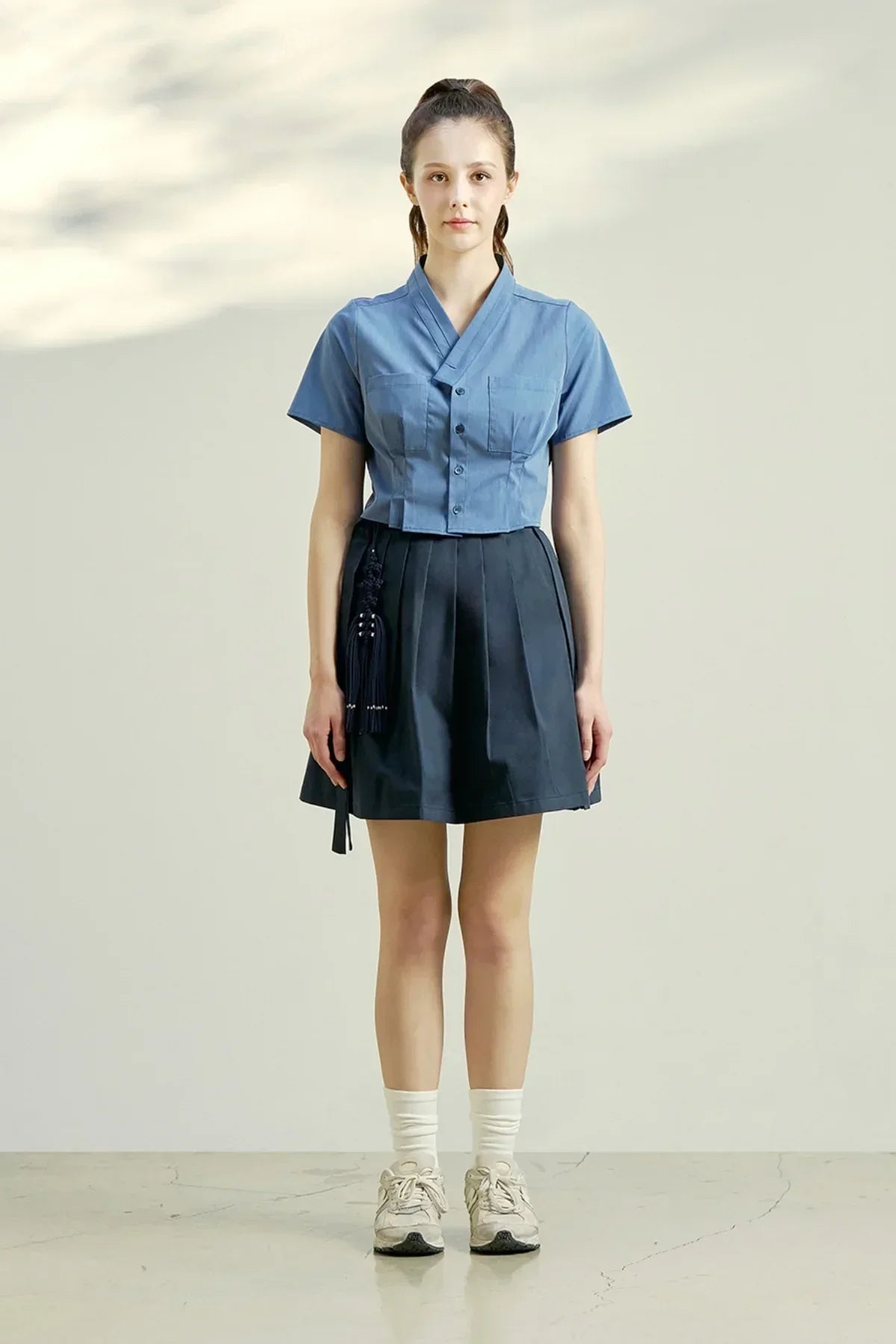 Model wearing indigo blue cropped blouse with buttons and navy pleated skirt with tassel detail