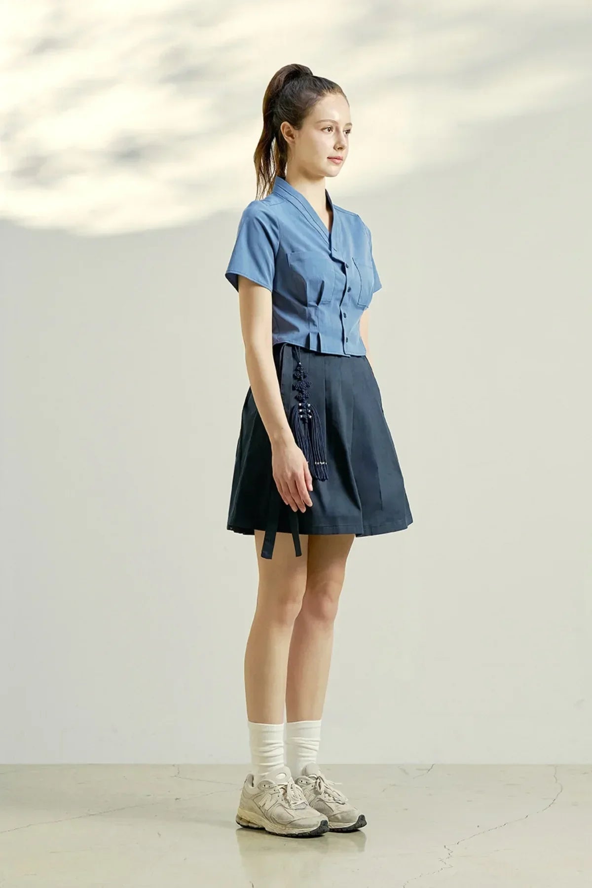 Model in indigo blue short-sleeve blouse paired with navy pleated skirt and cream sneakers