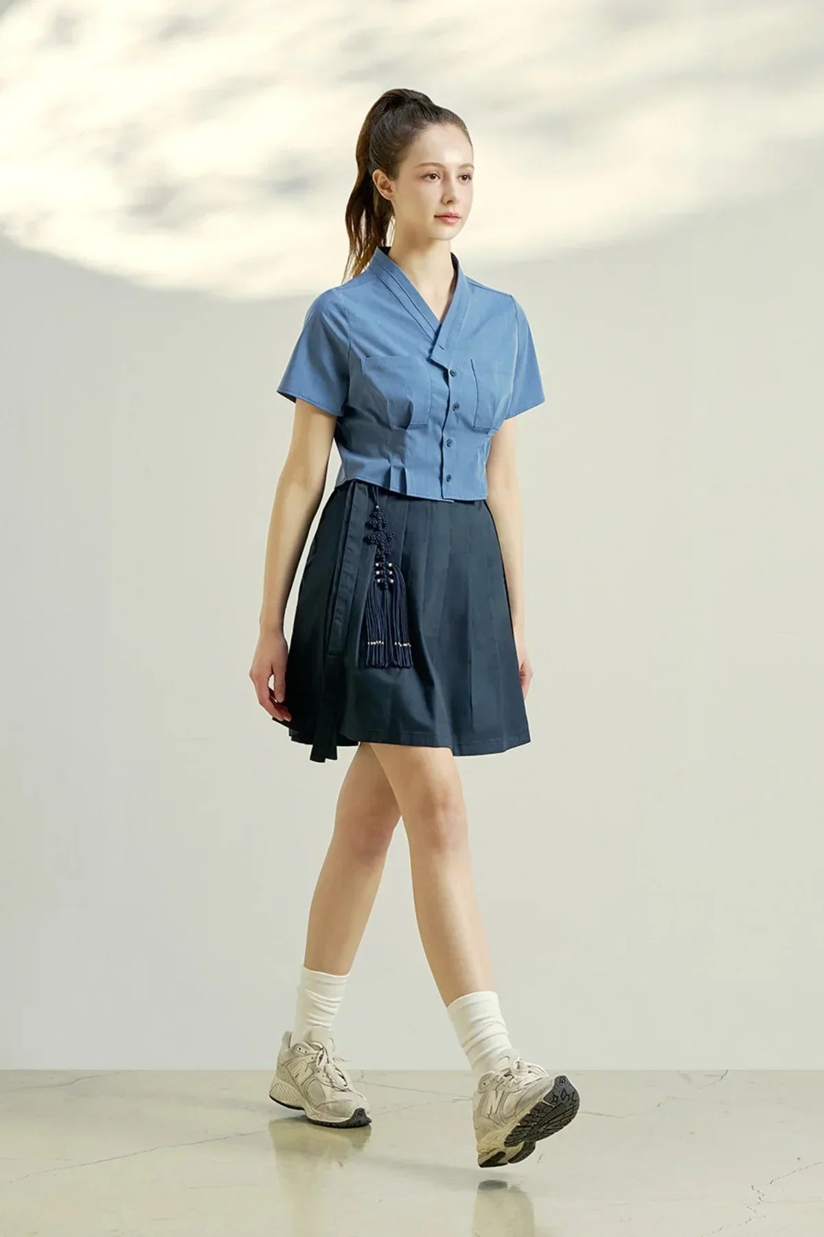 Woman wearing indigo blue cropped blouse and navy skirt with tassel detail walking indoors