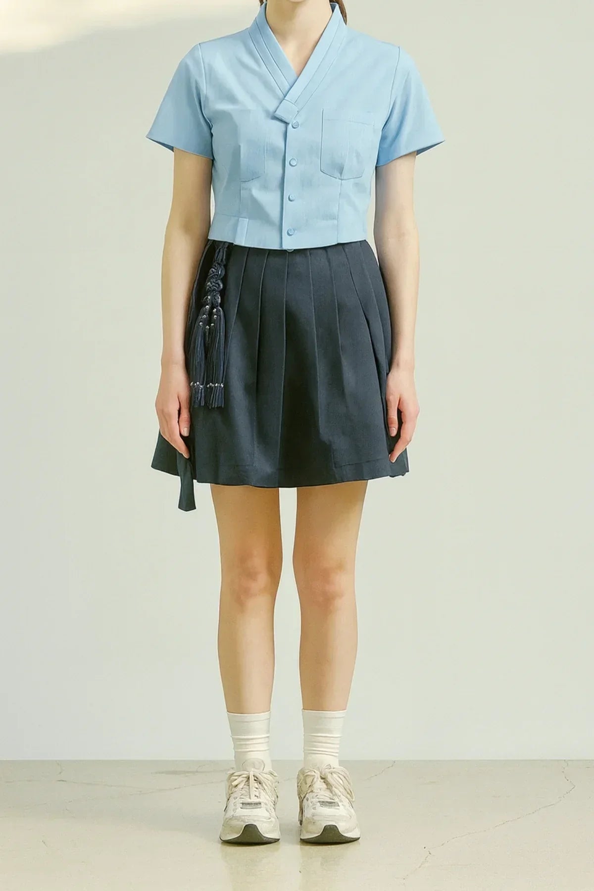 Woman in sky blue short sleeve blouse with a V-neck and navy pleated skirt with tassel detail
