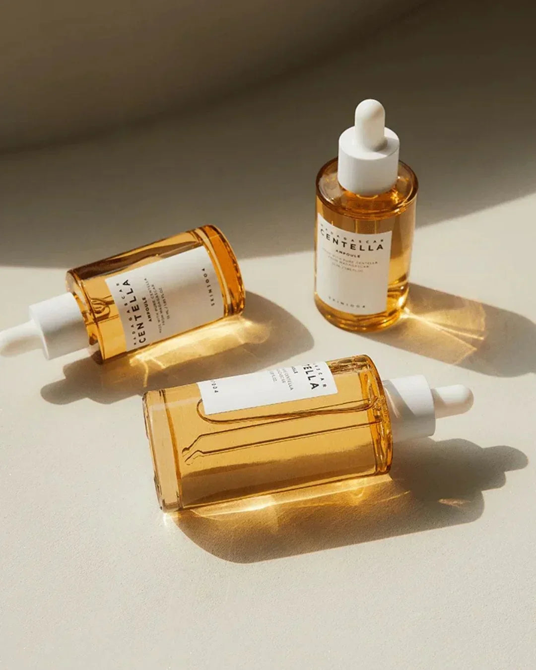 Three amber glass dropper bottles of Madagascar Centella Ampoule skincare on beige surface with natural light
