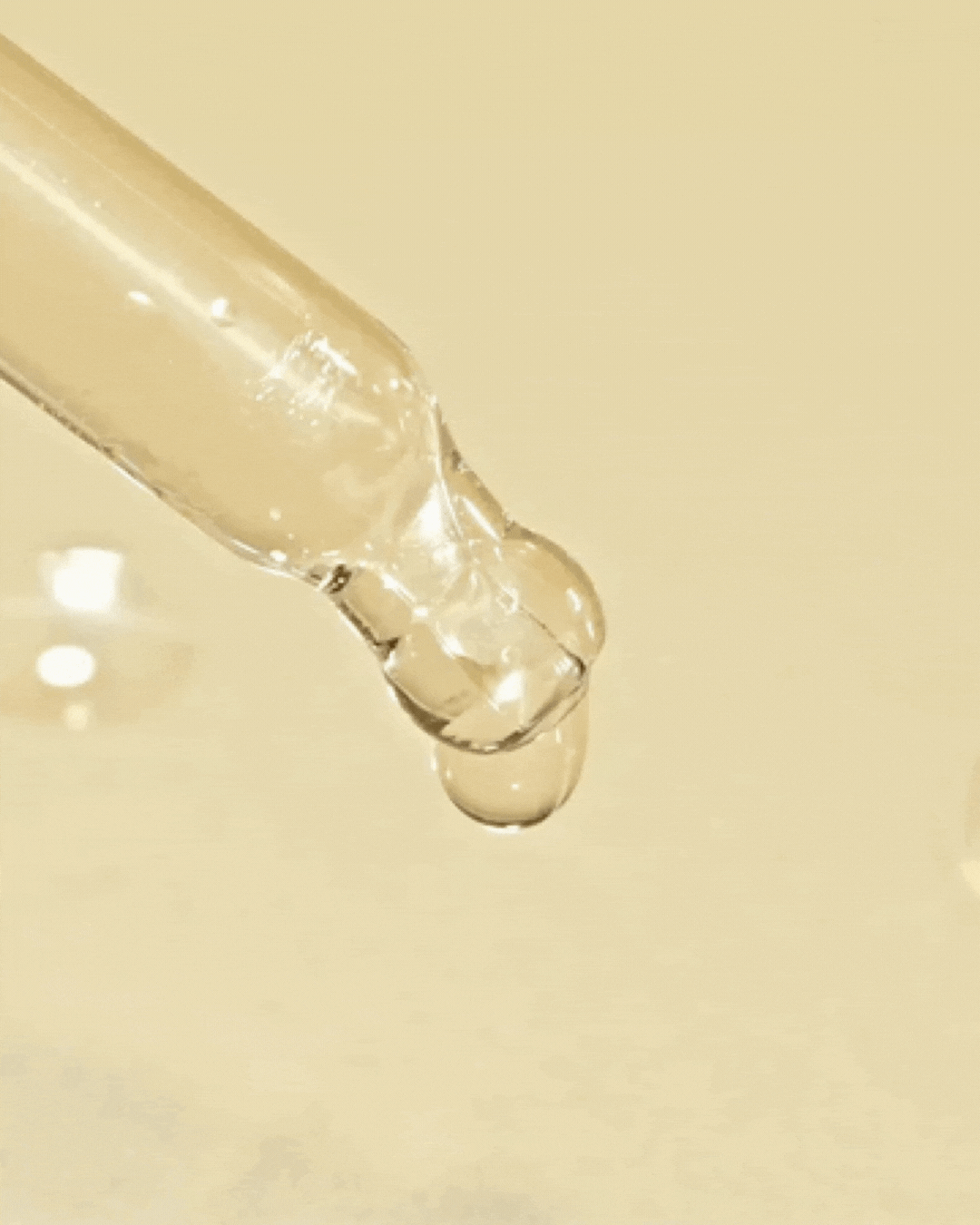 Close-up of clear serum liquid dripping from a glass dropper on beige background
