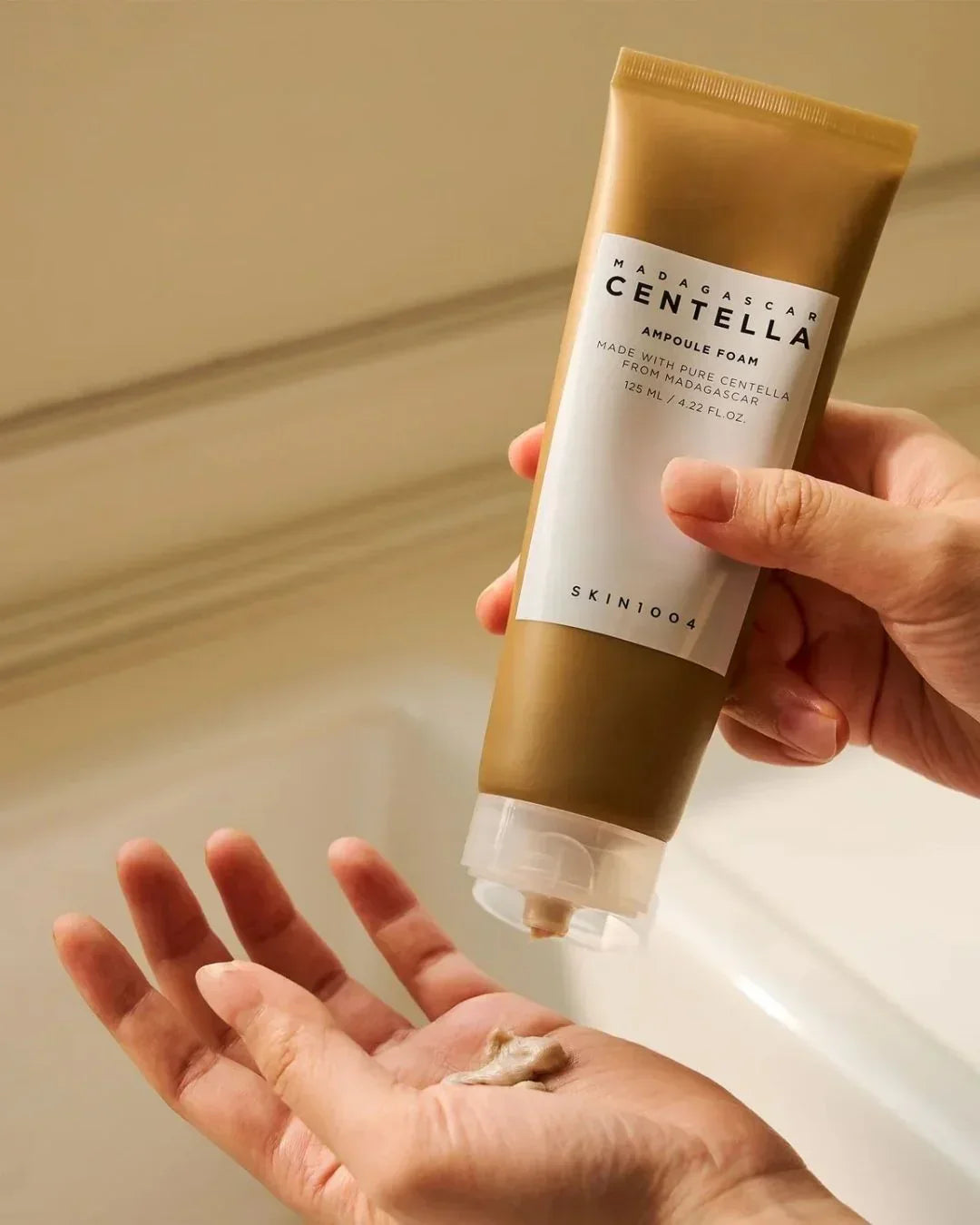 Hand holding Madagascar Centella Ampoule Foam skincare tube, dispensing foam onto palm