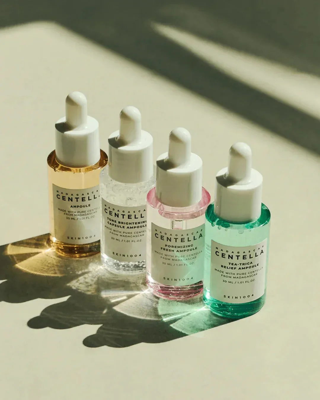 Four Madagascar Centella ampoules in yellow, clear, pink, and green with white droppers on light surface
