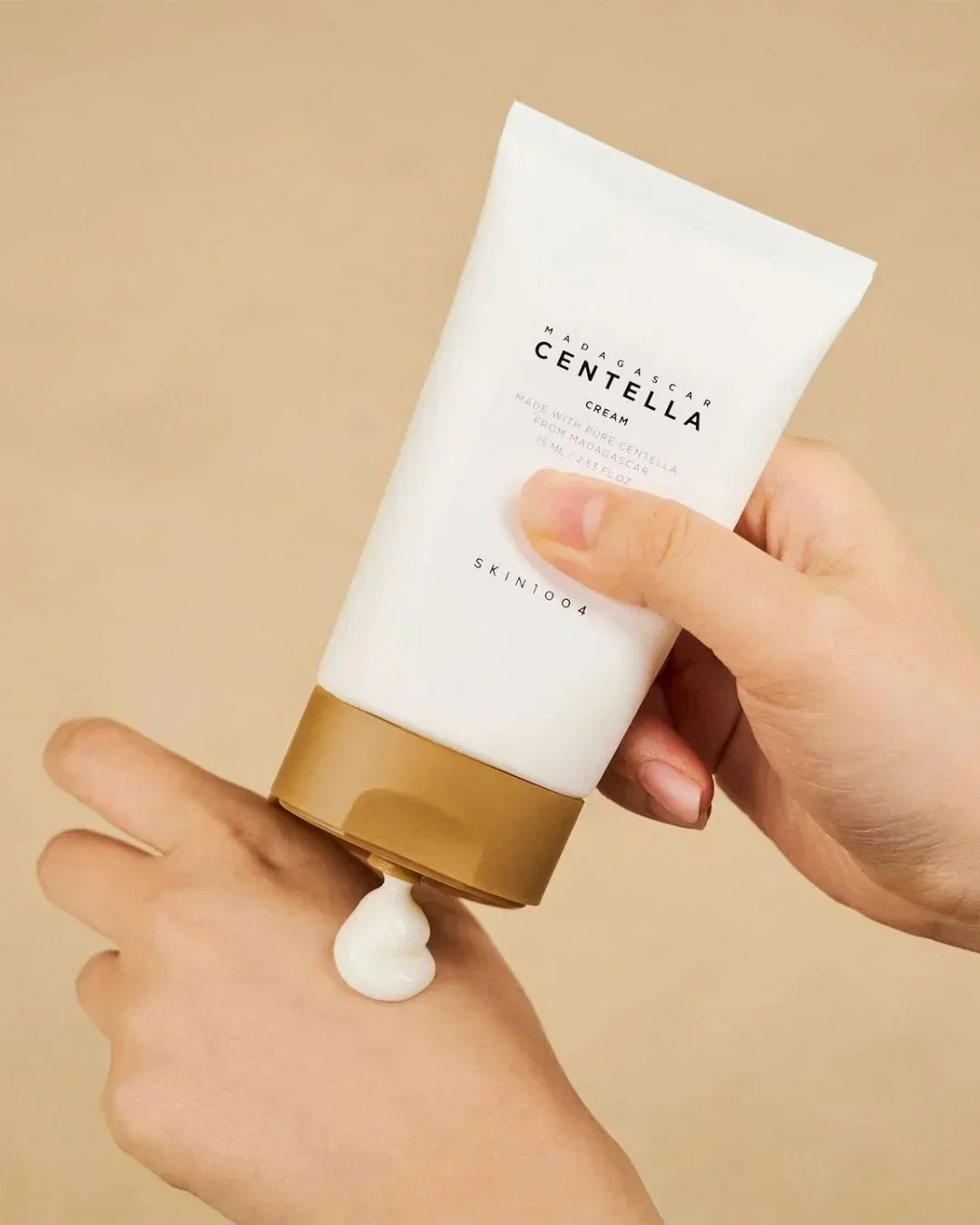 Hand applying Madagascar Centella cream from a white tube with brown cap onto skin