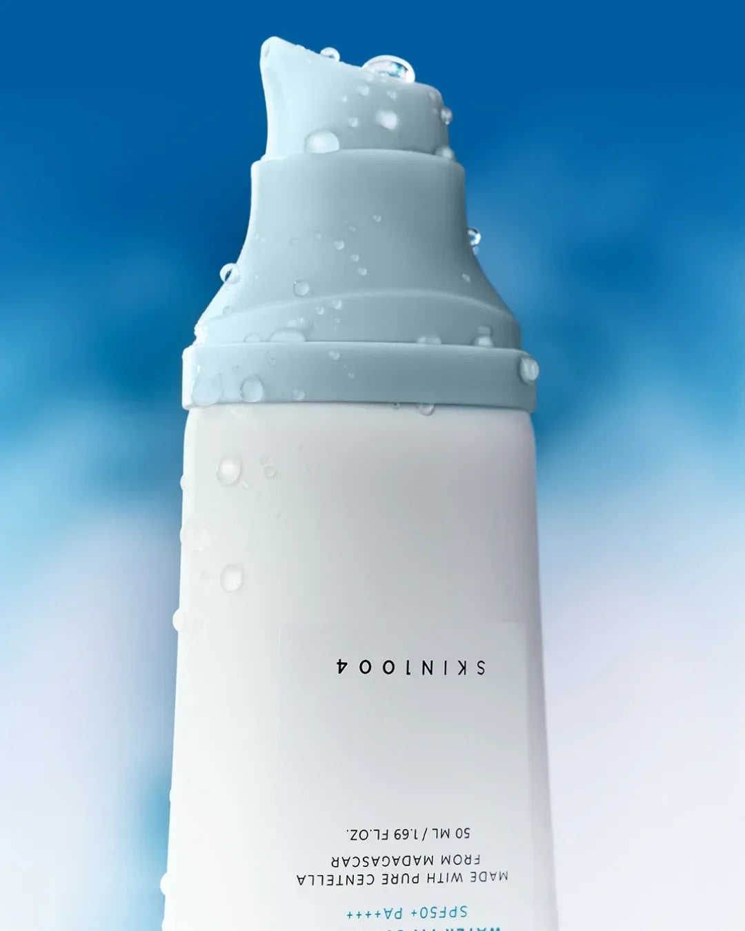 Close-up of white skincare serum bottle with gray pump and water droplets on blue background