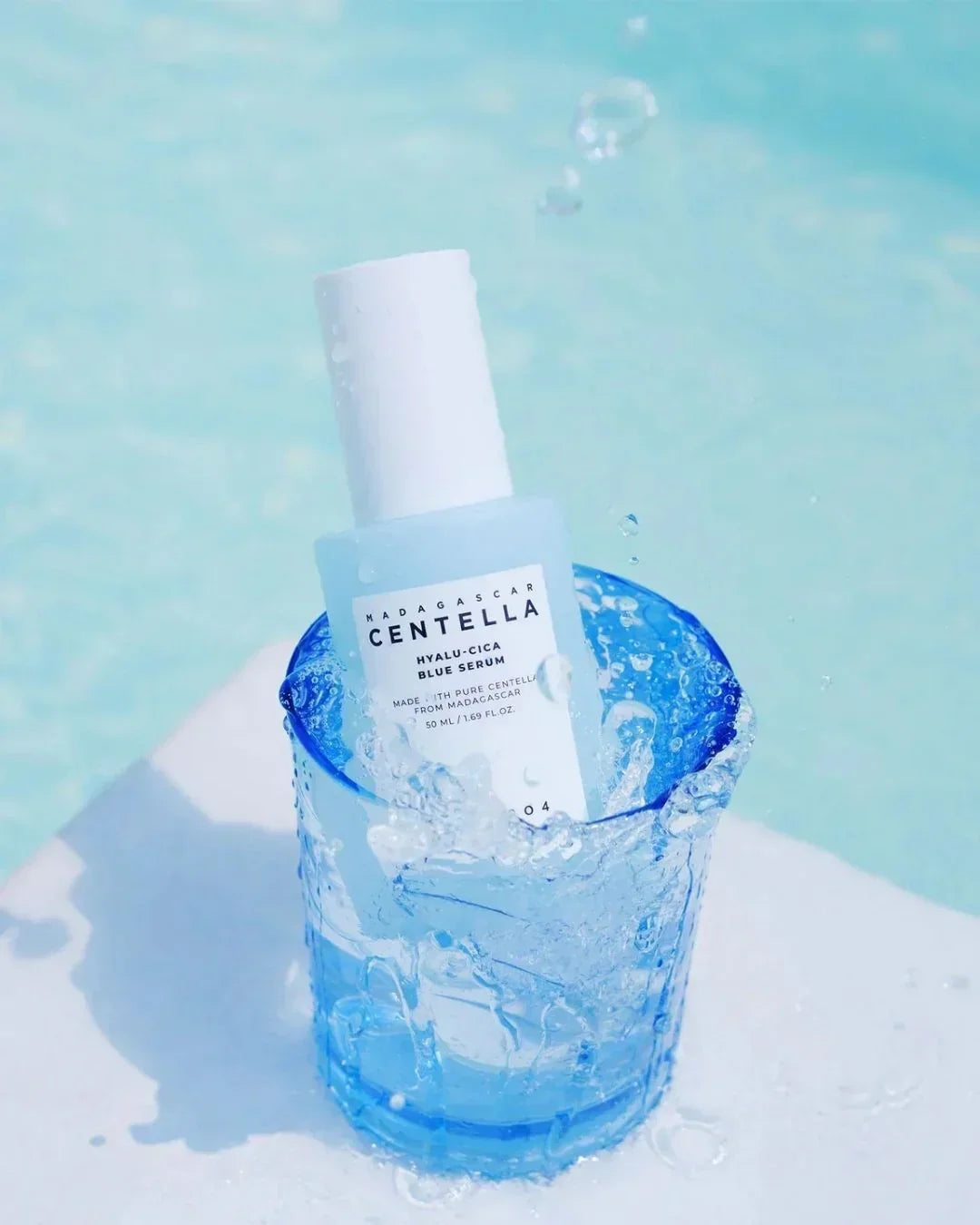 Madagascar Centella Hyalu-Cica Blue Serum bottle splashing in blue glass with water droplets