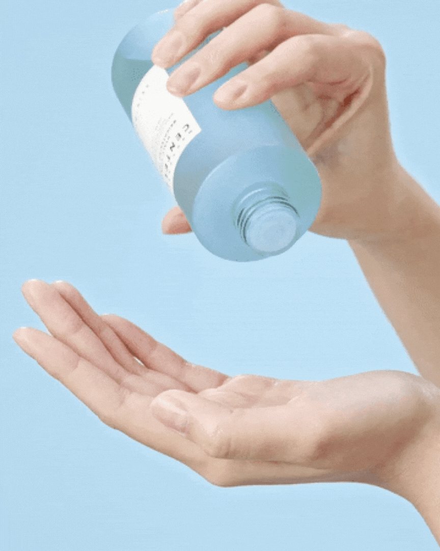 Hand pouring Madagascar Centella Hyalu Cica Brightening Toner from blue bottle on light blue background