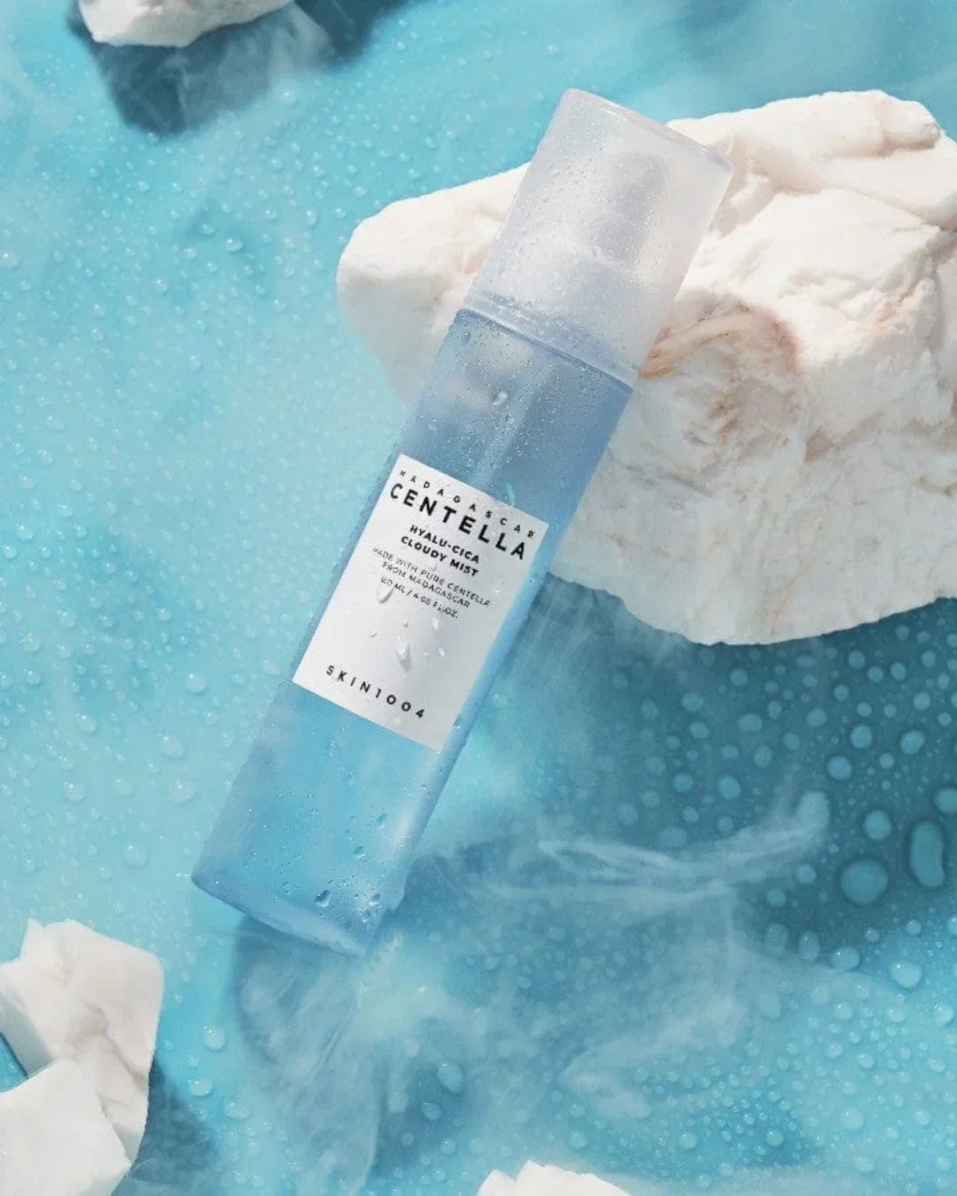 Skincare product Madagascar Centella Hyalu-Cica Cloudy Mist bottle on blue background with white stones