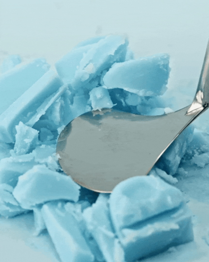 Close-up of a spoon scraping soft, crumbly blue skincare cream texture on a light surface