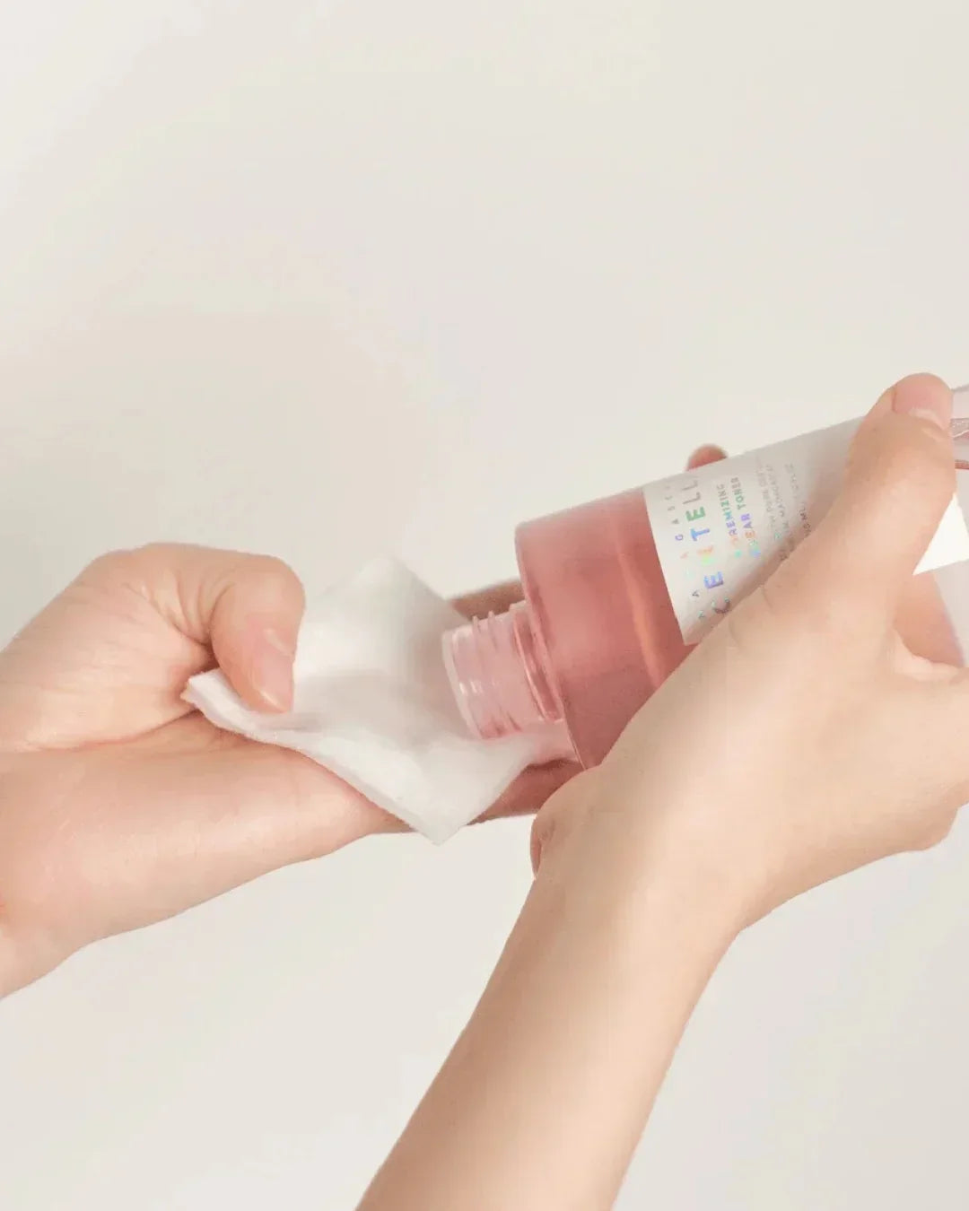 Hands pouring Madagascar Centella Poremizing Clear Toner onto cotton pad with neutral background