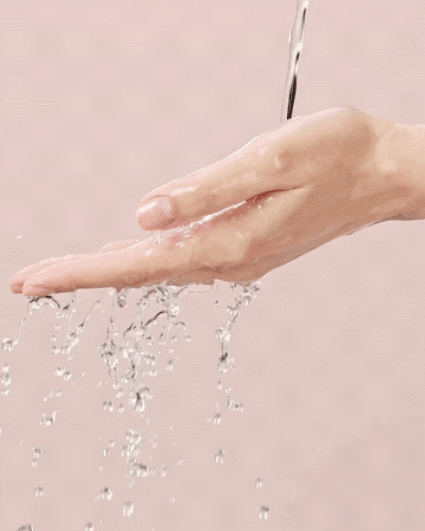 Close-up of water flowing over a clean hand against a soft pink background