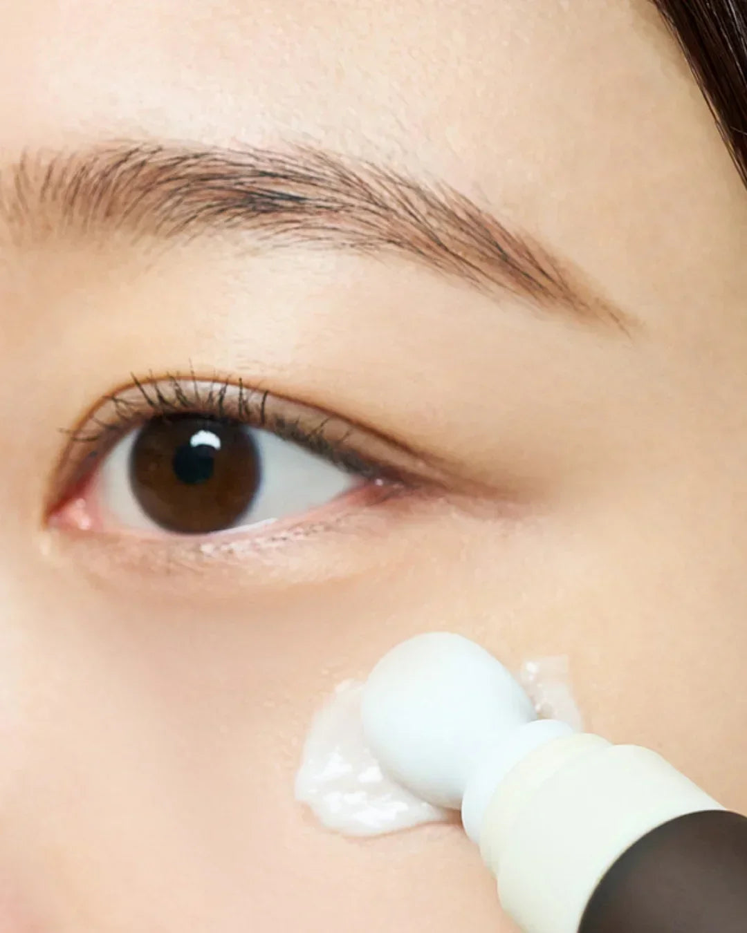 Close-up of applying Madagascar Centella eye cream with rollerball on under-eye skin