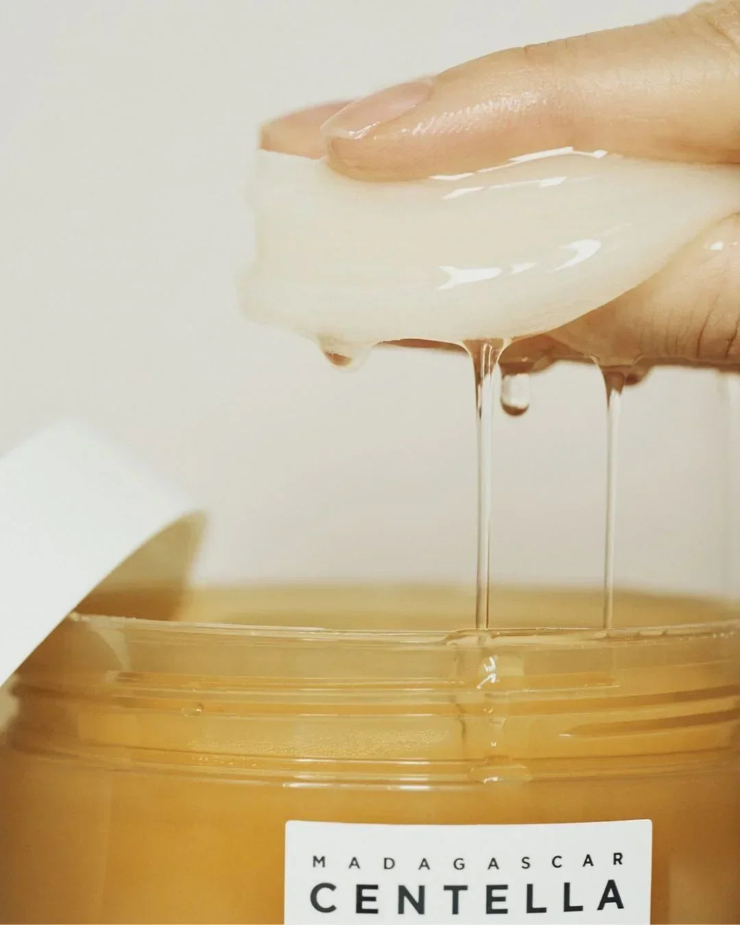 Hand squeezing clear gel from white pad over jar labeled Madagascar Centella skincare