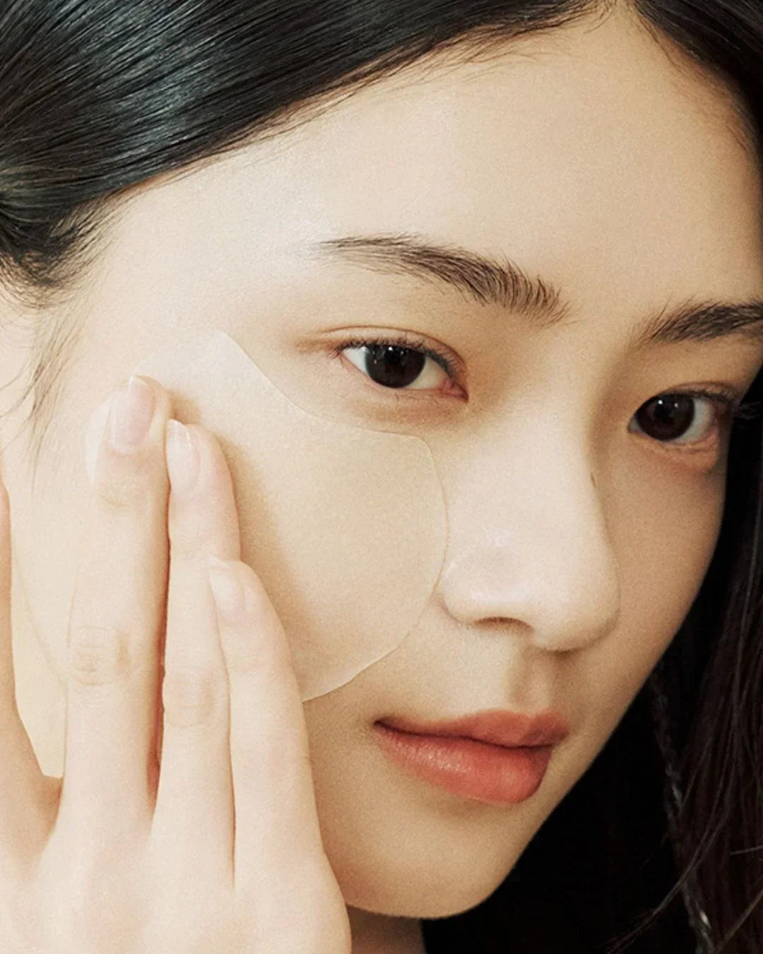 Close-up of woman applying transparent centella calming pad on cheek for skincare