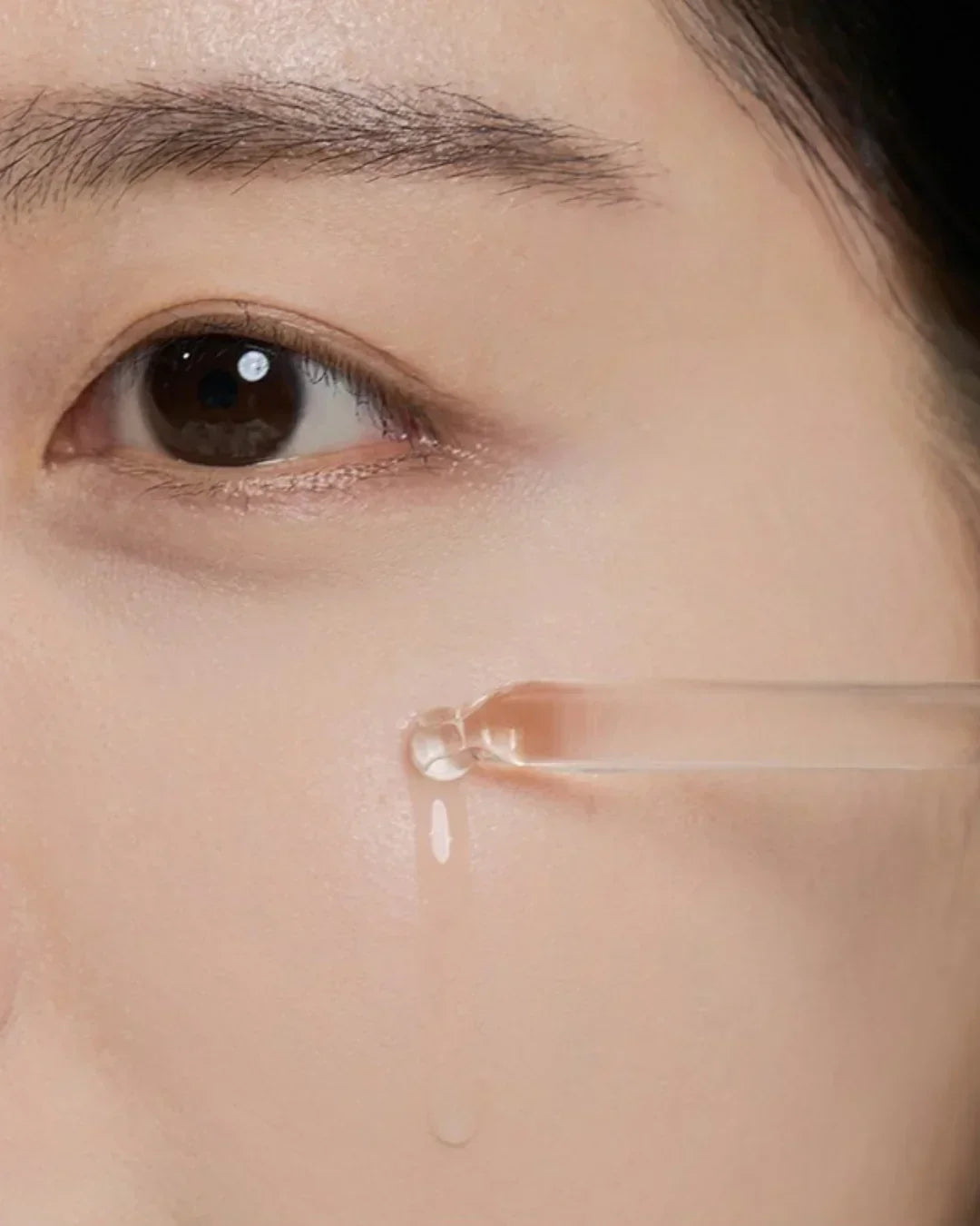 Close-up of woman's cheek with clear serum drop from pipette, highlighting skincare application