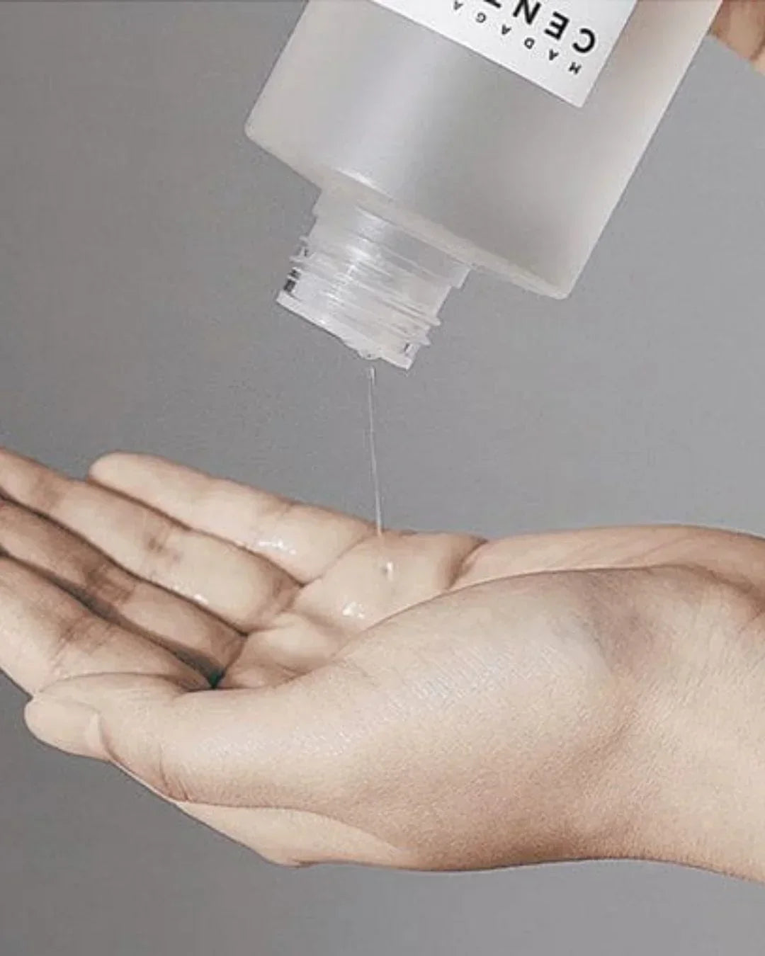 Madagascar Centella Tone Brightening Boosting Toner pouring liquid into a person's palm against gray background