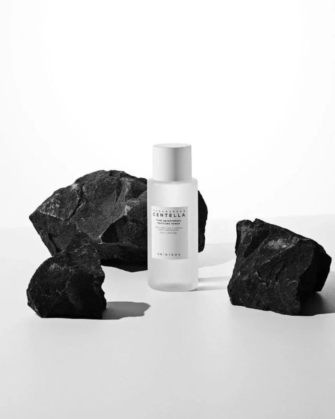 Madagascar Centella Tone Brightening Boosting Toner bottle on white surface with black rocks
