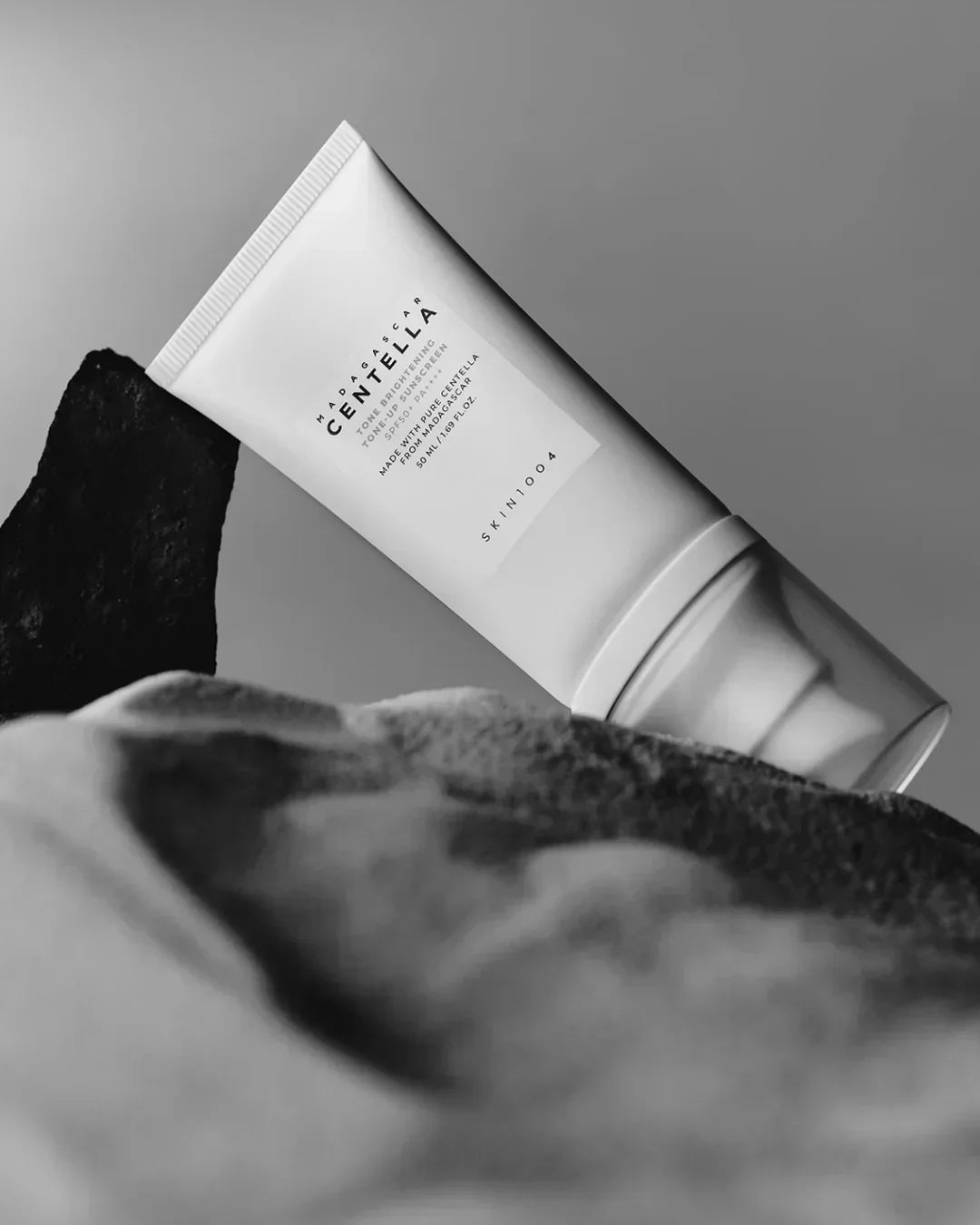 Madagascar Centella tone brightening sunscreen tube with SPF 50 on textured stones in black and white
