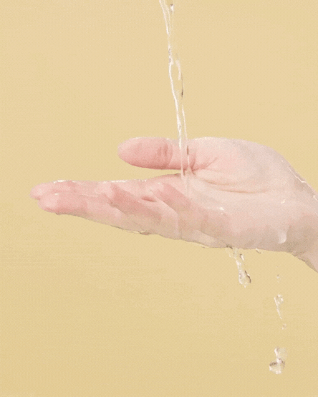 Hand catching clear liquid pouring against a beige background, highlighting toner texture