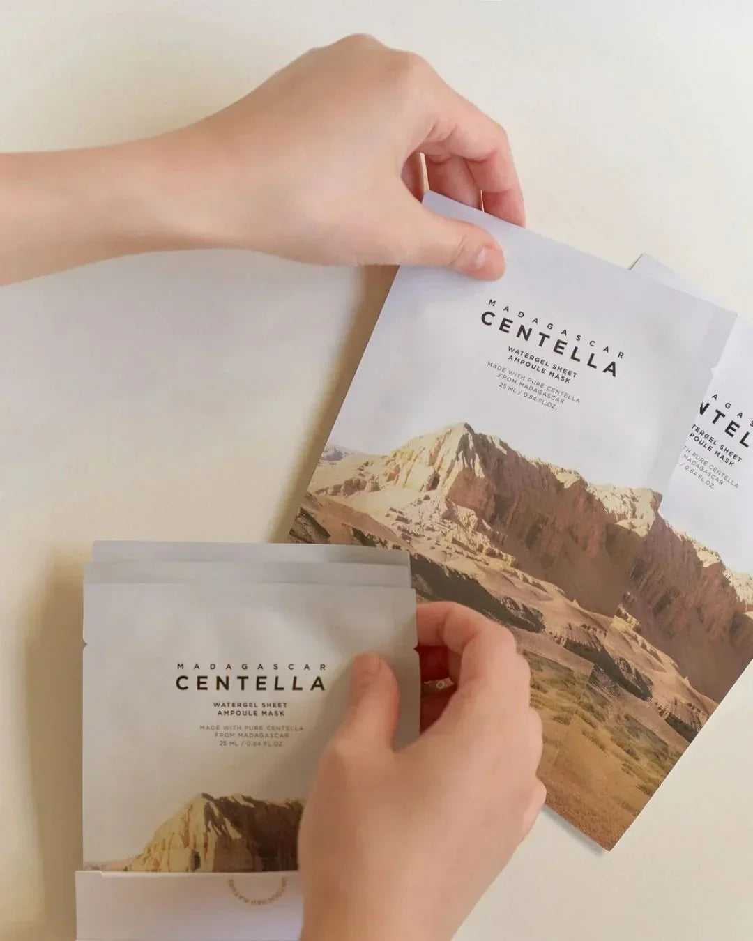 Hands holding Madagascar Centella Watergel Sheet Ampoule Mask packets with mountain design
