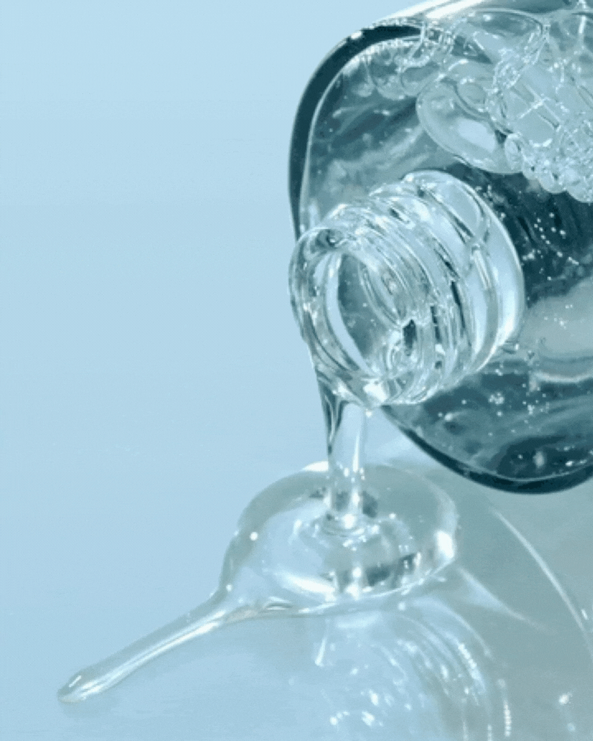 Clear hydrating serum pouring from a glass bottle with a smooth gel texture on a pale blue surface