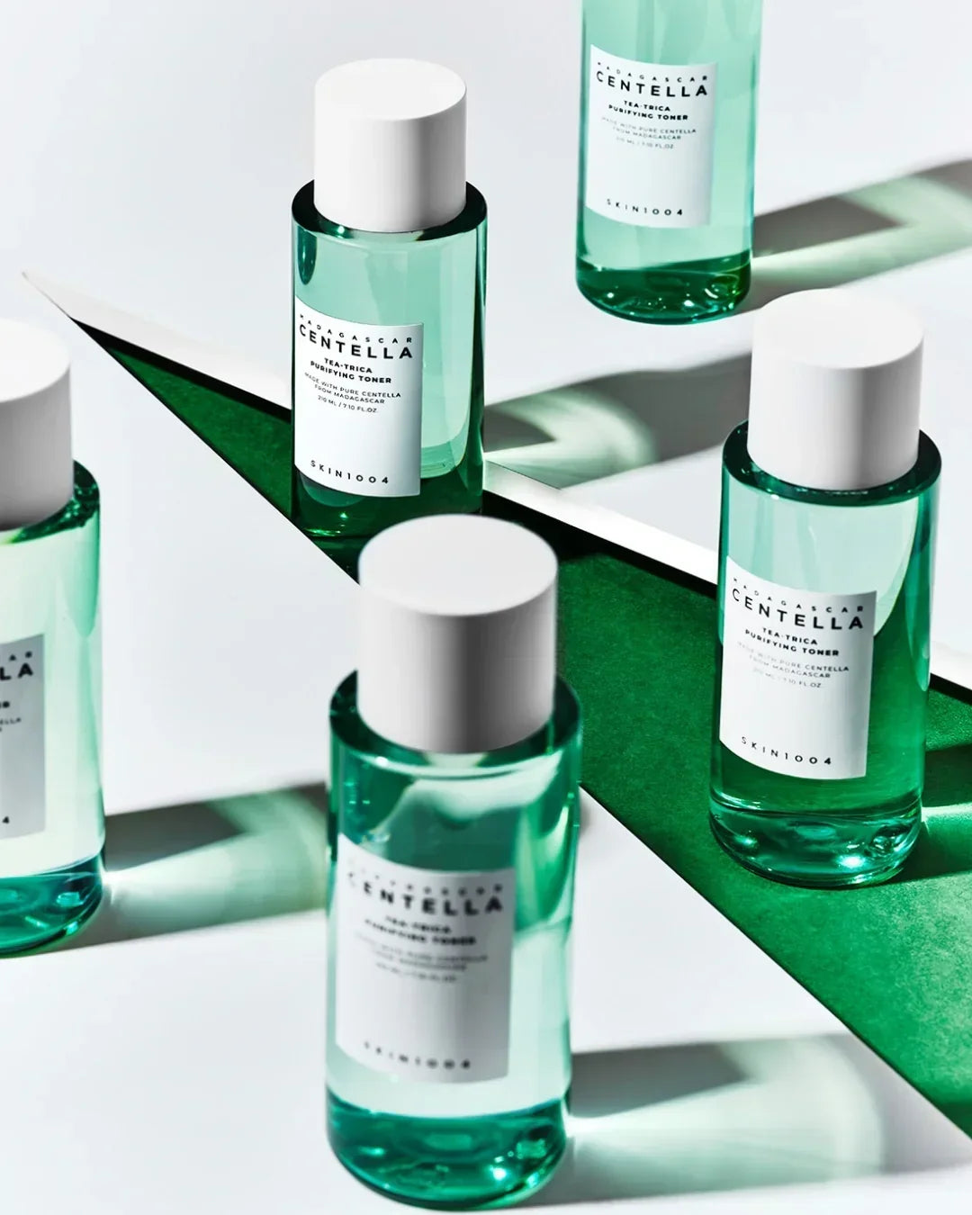 Multiple bottles of Madagascar Centella Tea-Trica Purifying Toner by Skin1004 on white and green mirrored surfaces