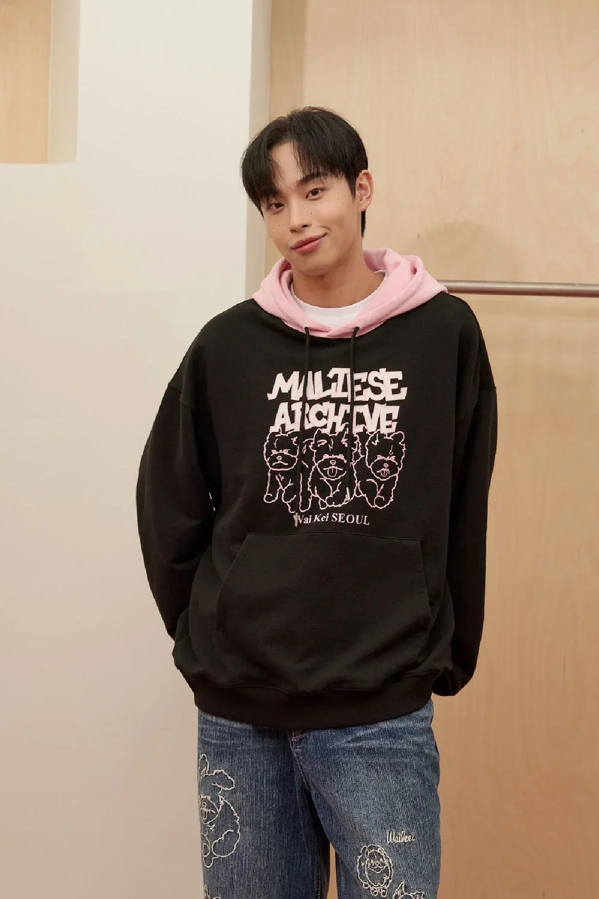 Young man wearing black and pink Maltese Archive graphic hoodie with blue jeans featuring dog prints