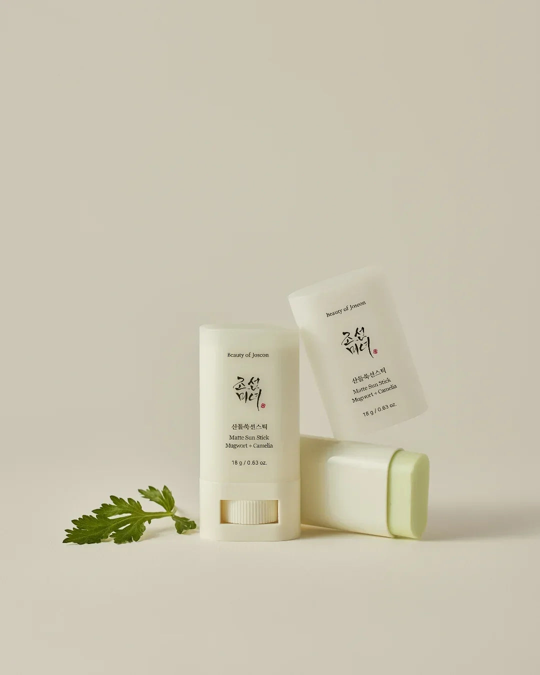Matte Sun Stick Mugwort and Camellia sunscreen products with Korean text and a green leaf on beige background