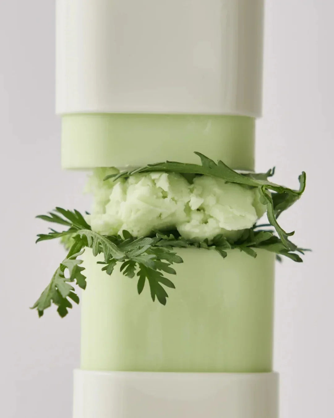 Close-up of green matte sun stick with mugwort leaves and soft texture in white container