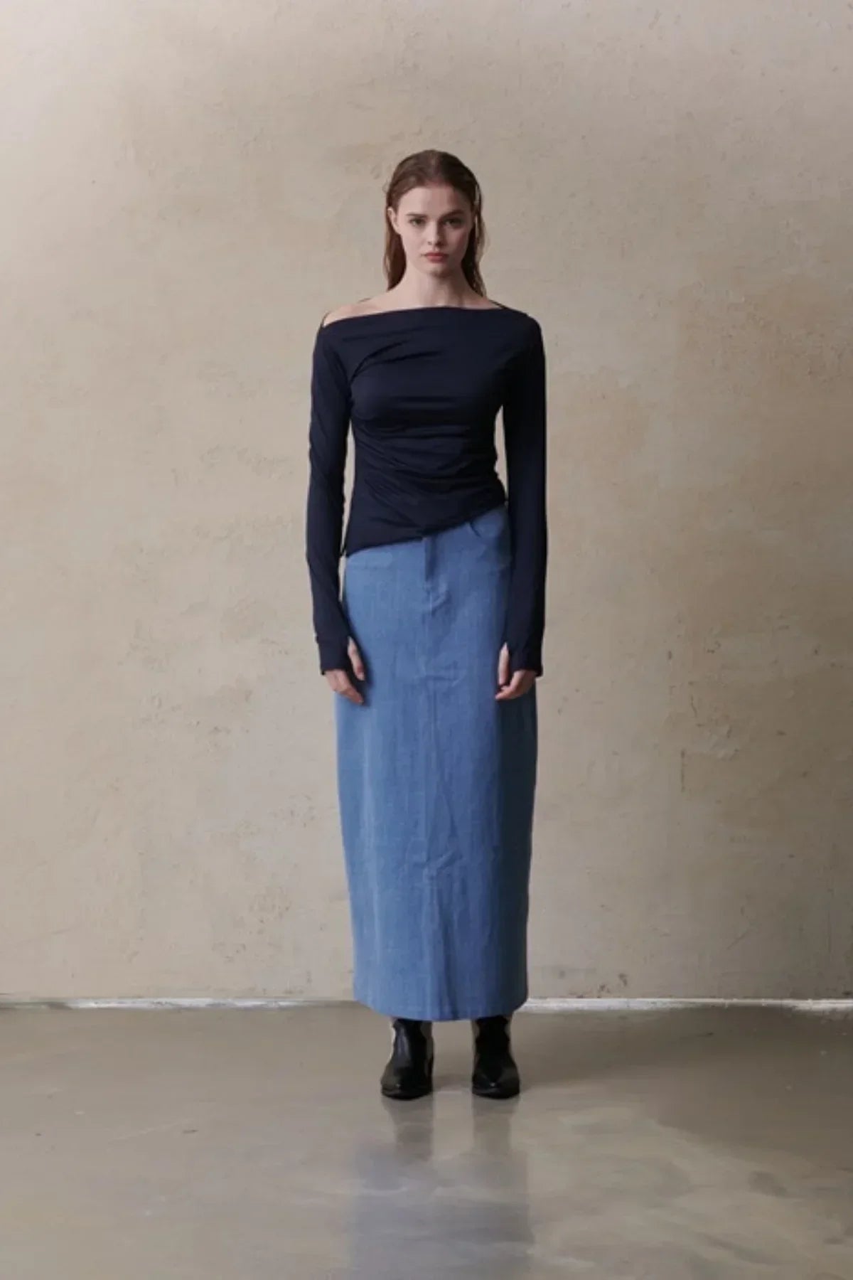 Model wearing mid-blue maxi denim skirt with black off-shoulder long-sleeve top and black boots