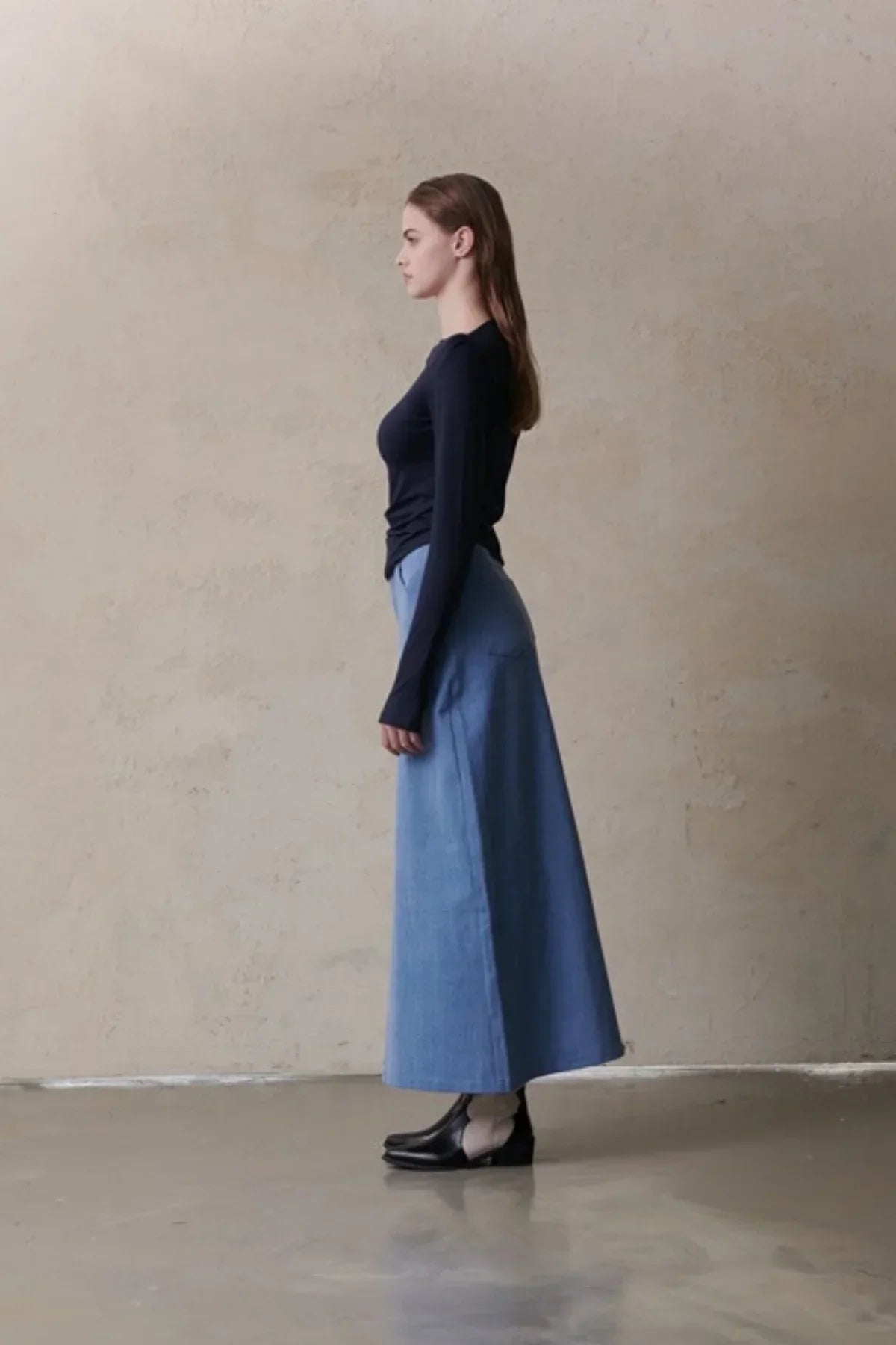 Woman wearing a mid-blue maxi denim skirt with a fitted long-sleeve black top and black ankle boots