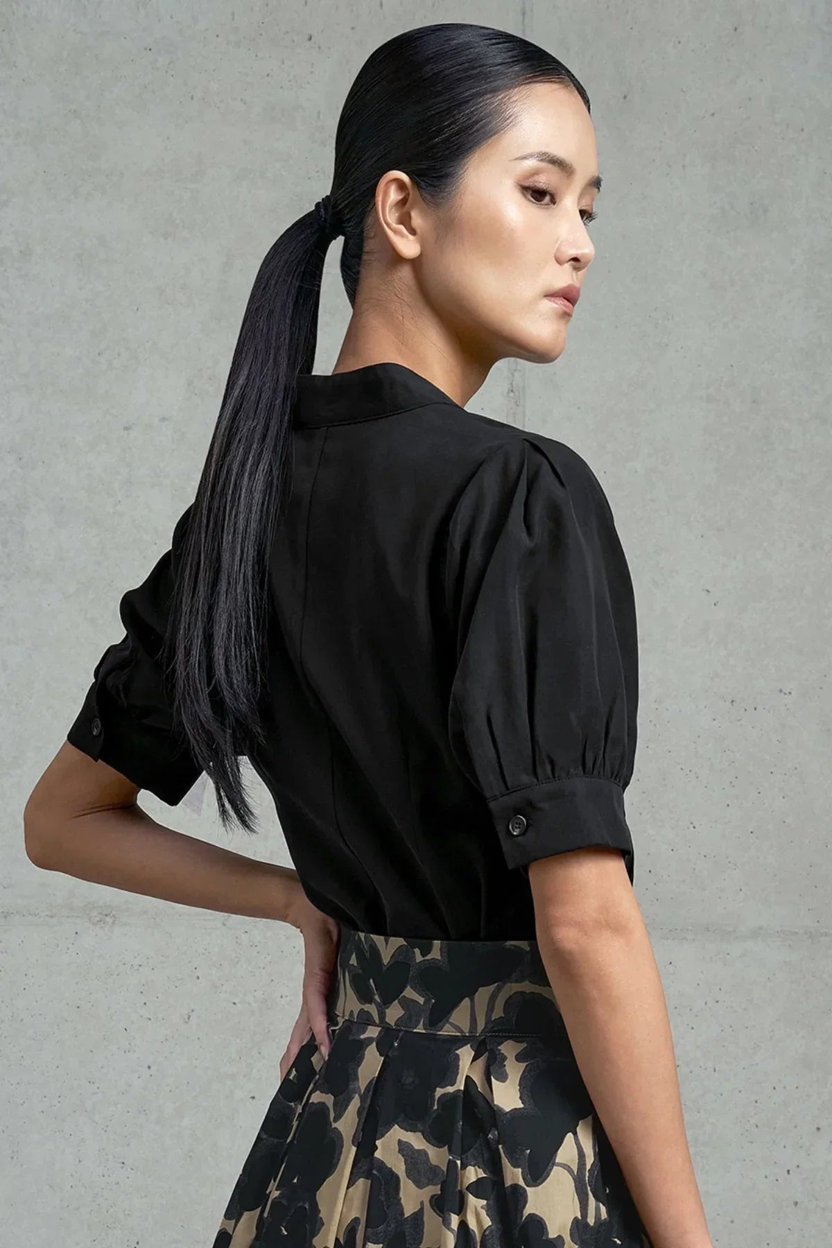 close-up of woman wearing black puff-sleeve blouse and floral patterned skirt against gray wall