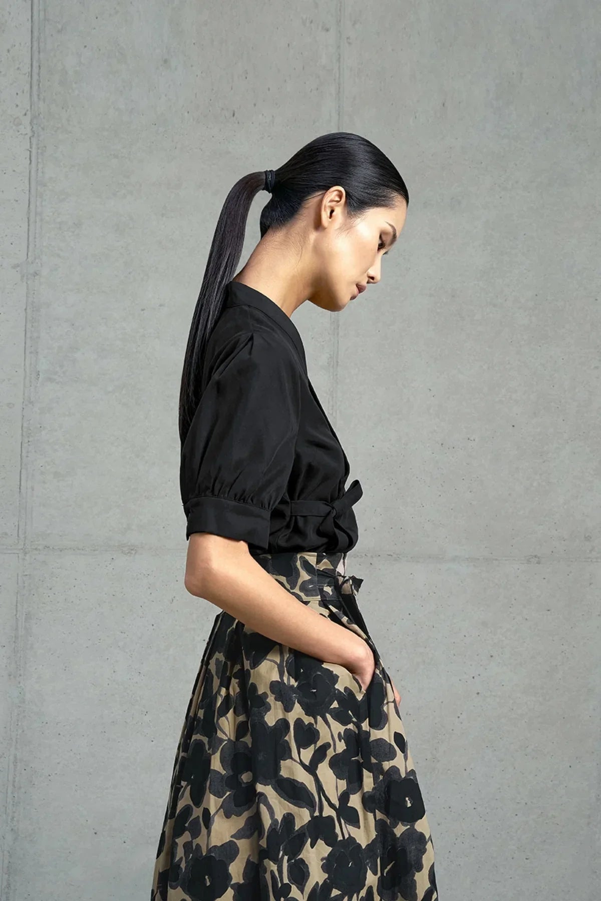 Side view of woman with sleek ponytail wearing black puff sleeve blouse and beige skirt with black floral print