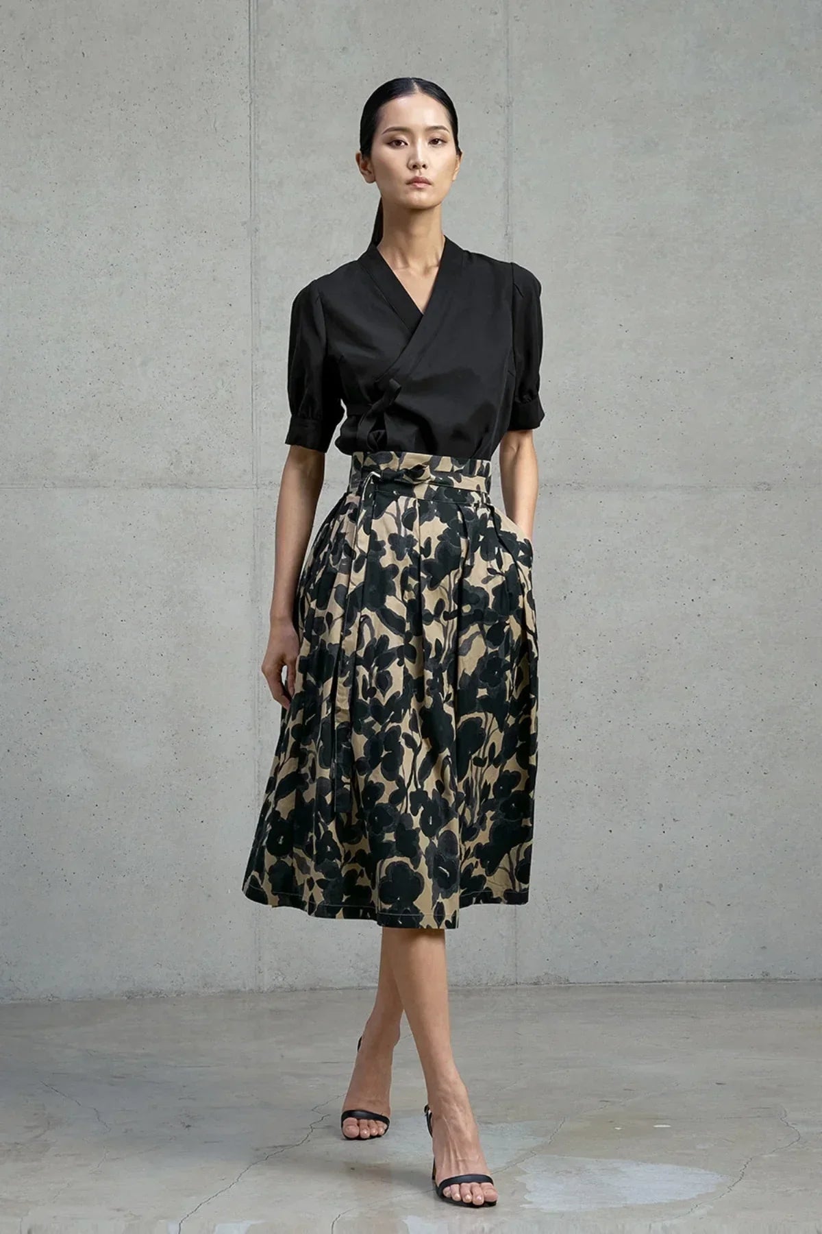 Model wearing black wrap blouse with puff sleeves and floral print midi skirt in studio