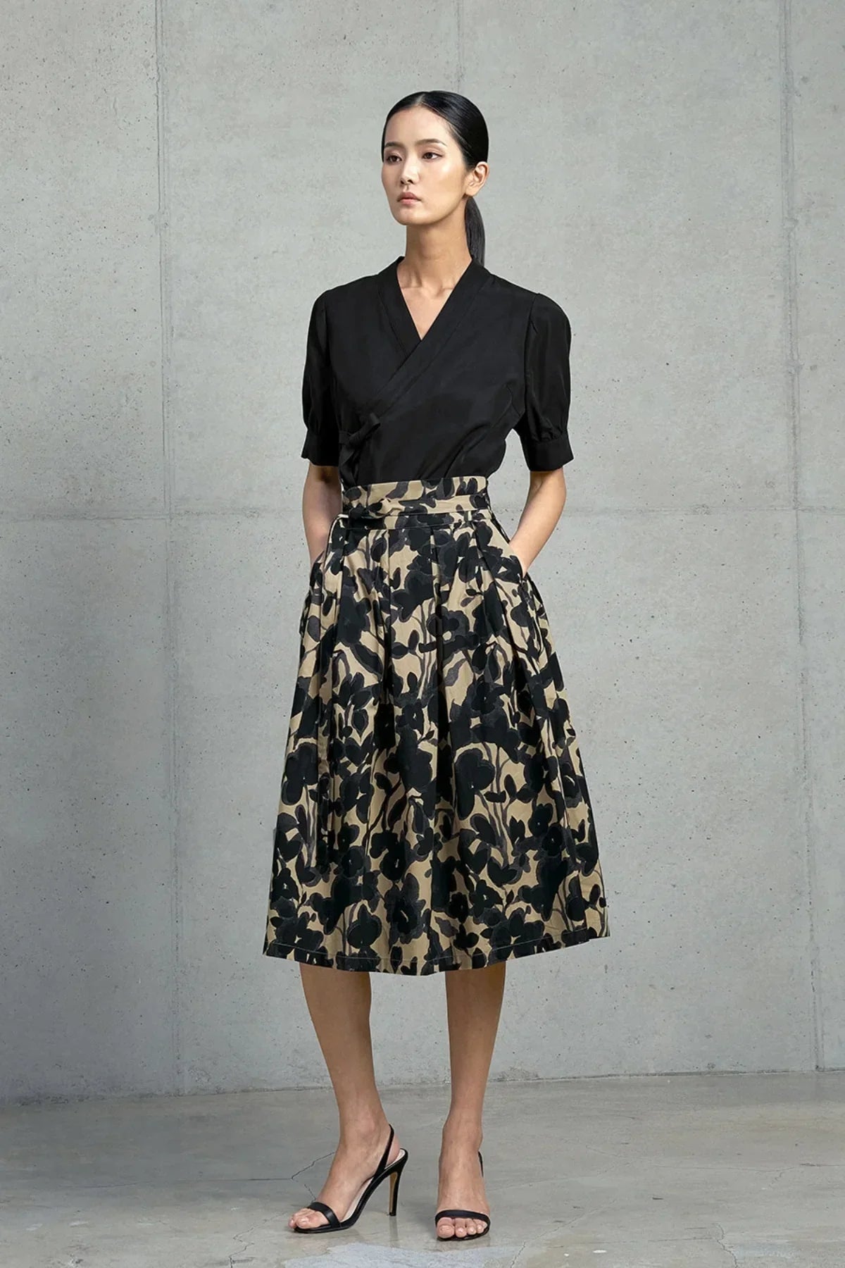 Woman in black wrap blouse and high-waist floral midi skirt posing against concrete wall