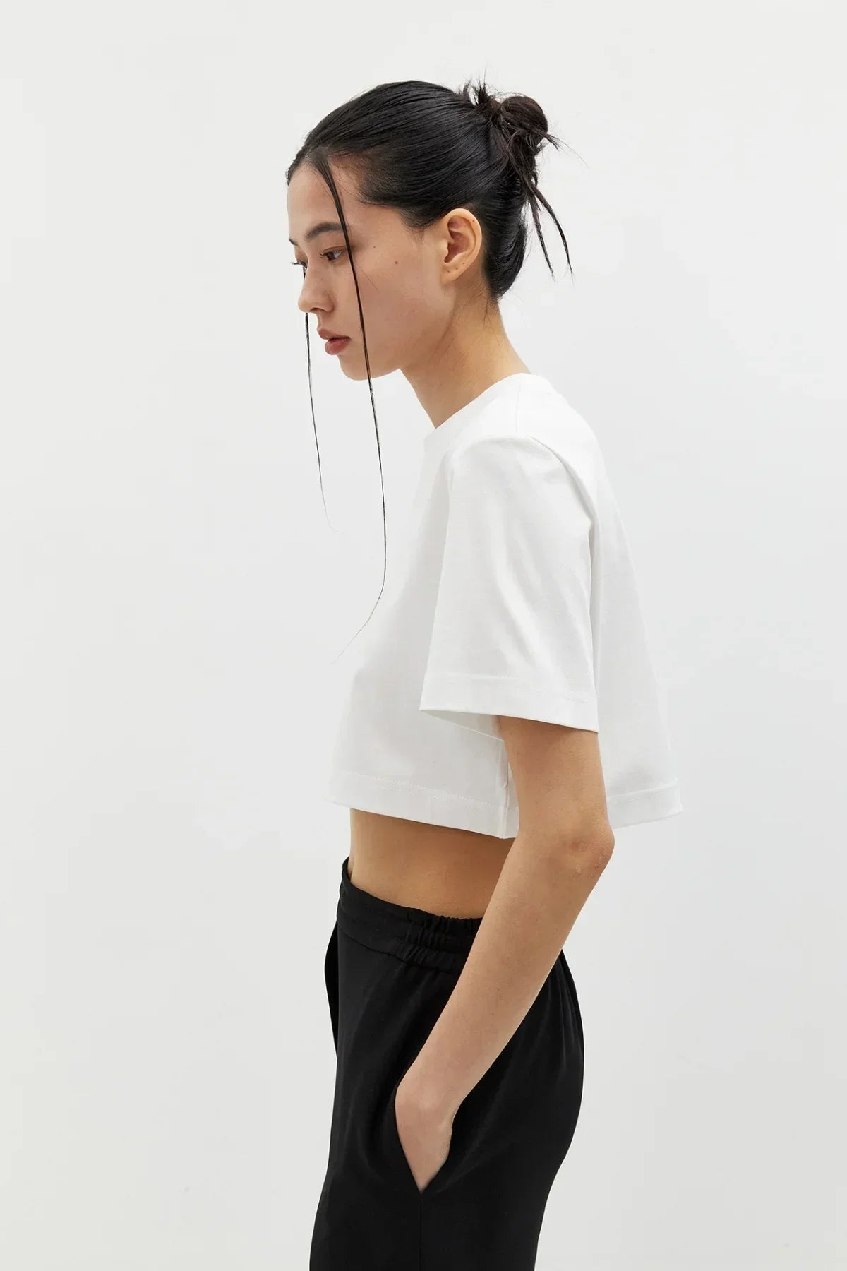 Side view of woman wearing white cropped t-shirt and black elastic waist pants against plain white background